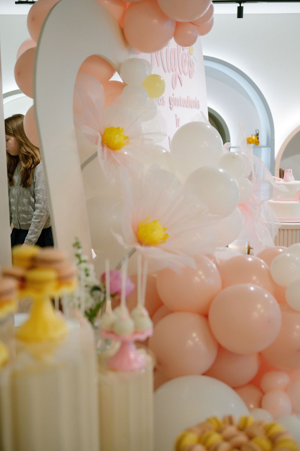 Pink balloon arch with daisy decorations and dessert table at a girls birthday party celebration.
