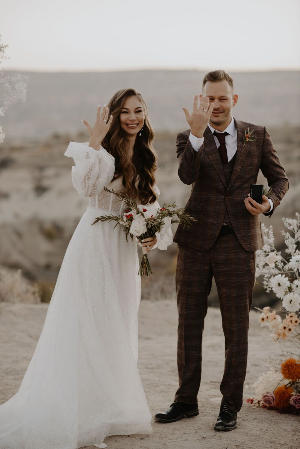 Bride and groom showing wedding rings outdoors in desert landscape after ceremony.