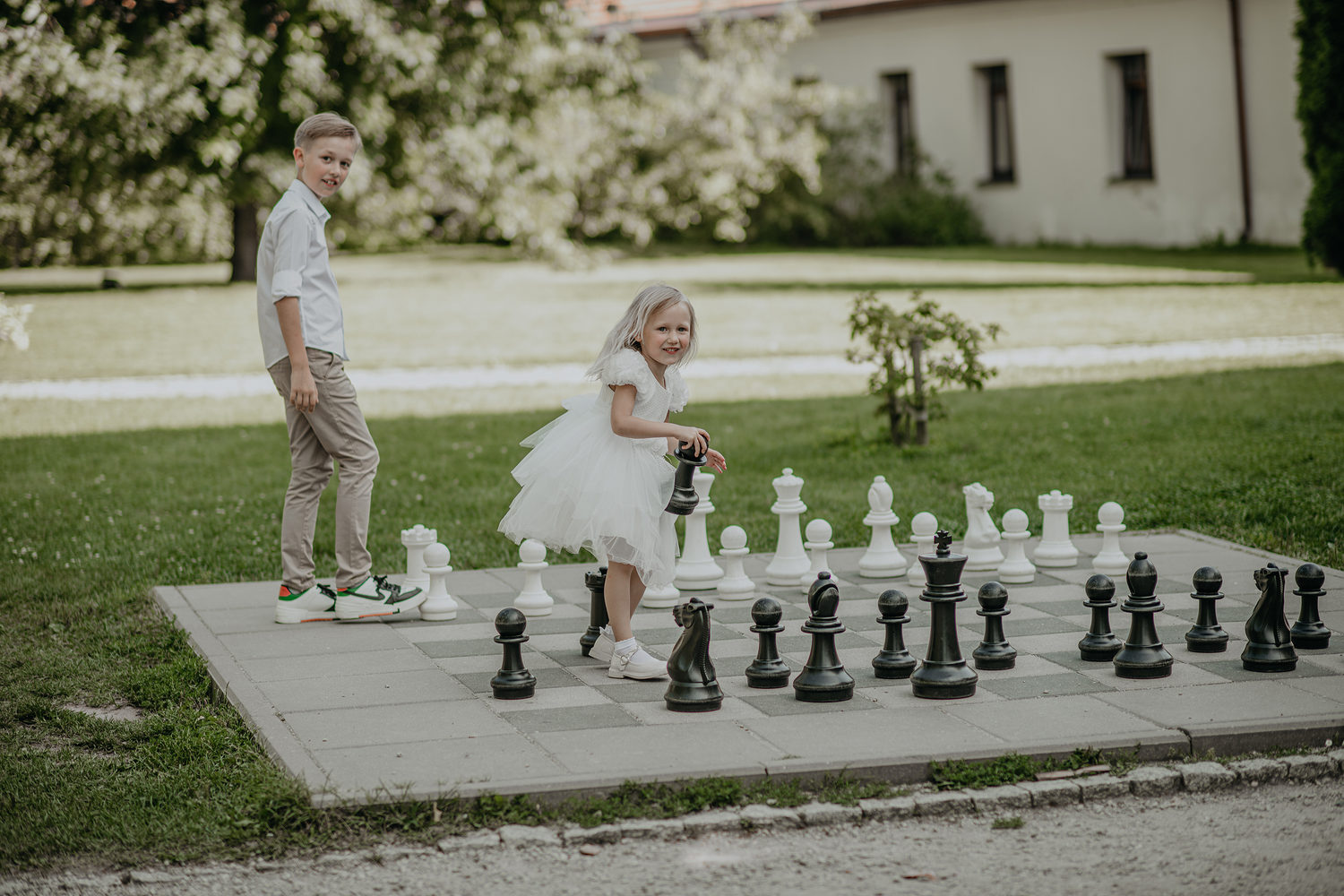 People playing chess on a large outdoor board with life-sized pieces in a park setting.