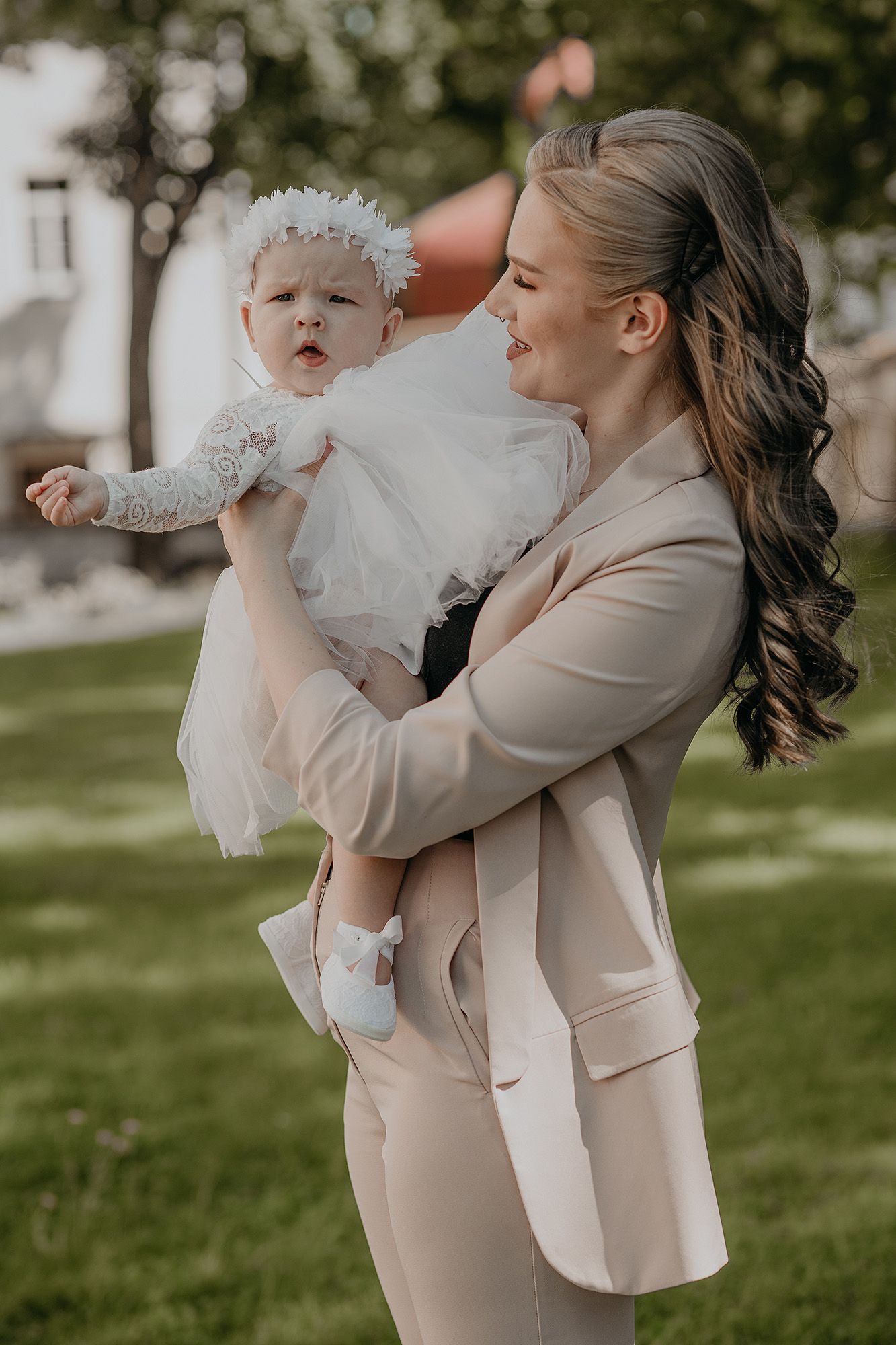 Mother and baby in matching cream outfits share tender moments outdoors on a sunny day.