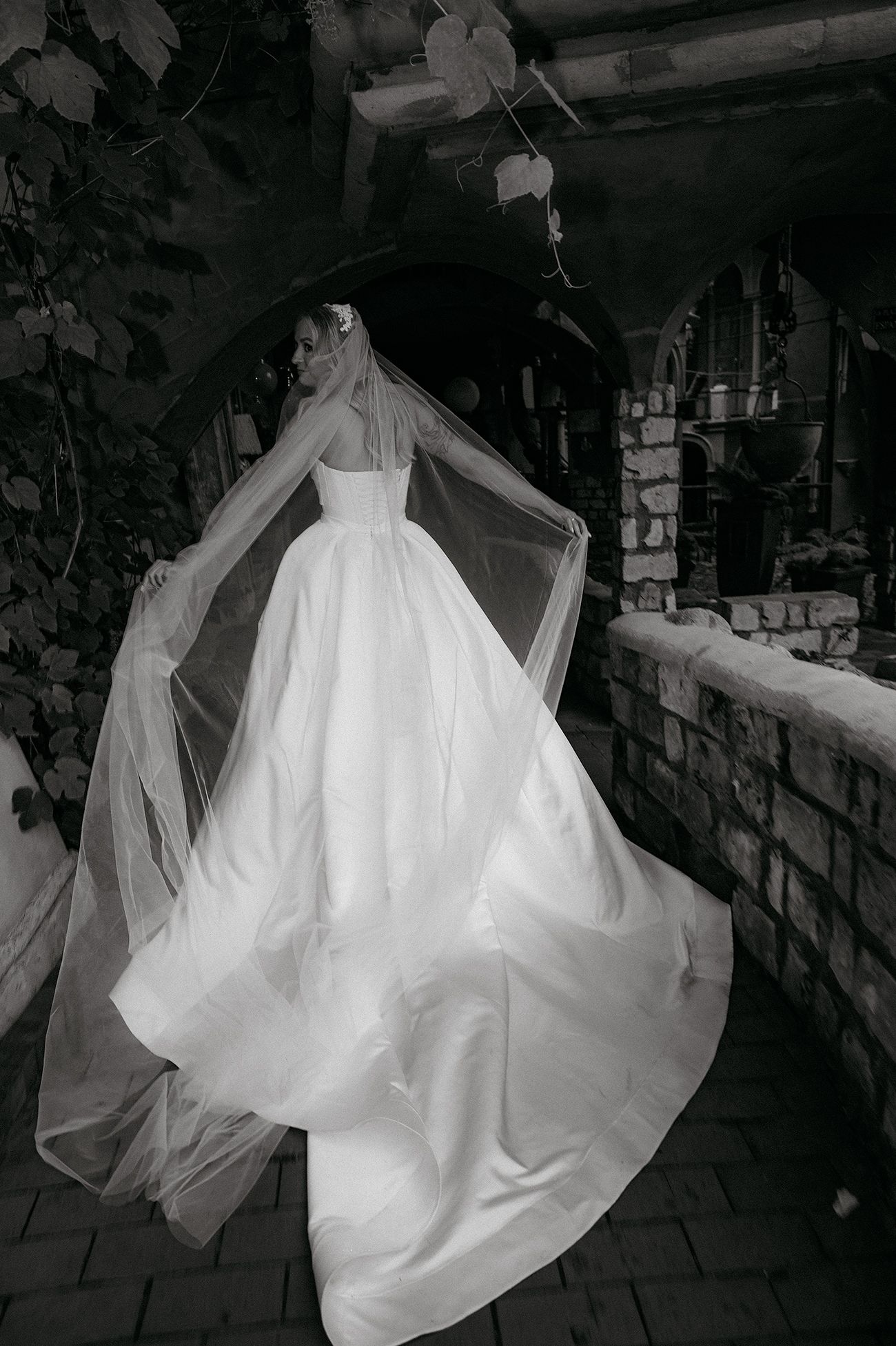 A flowing white wedding dress twirls gracefully against a dark stone wall background in a dramatic black and white photo series.