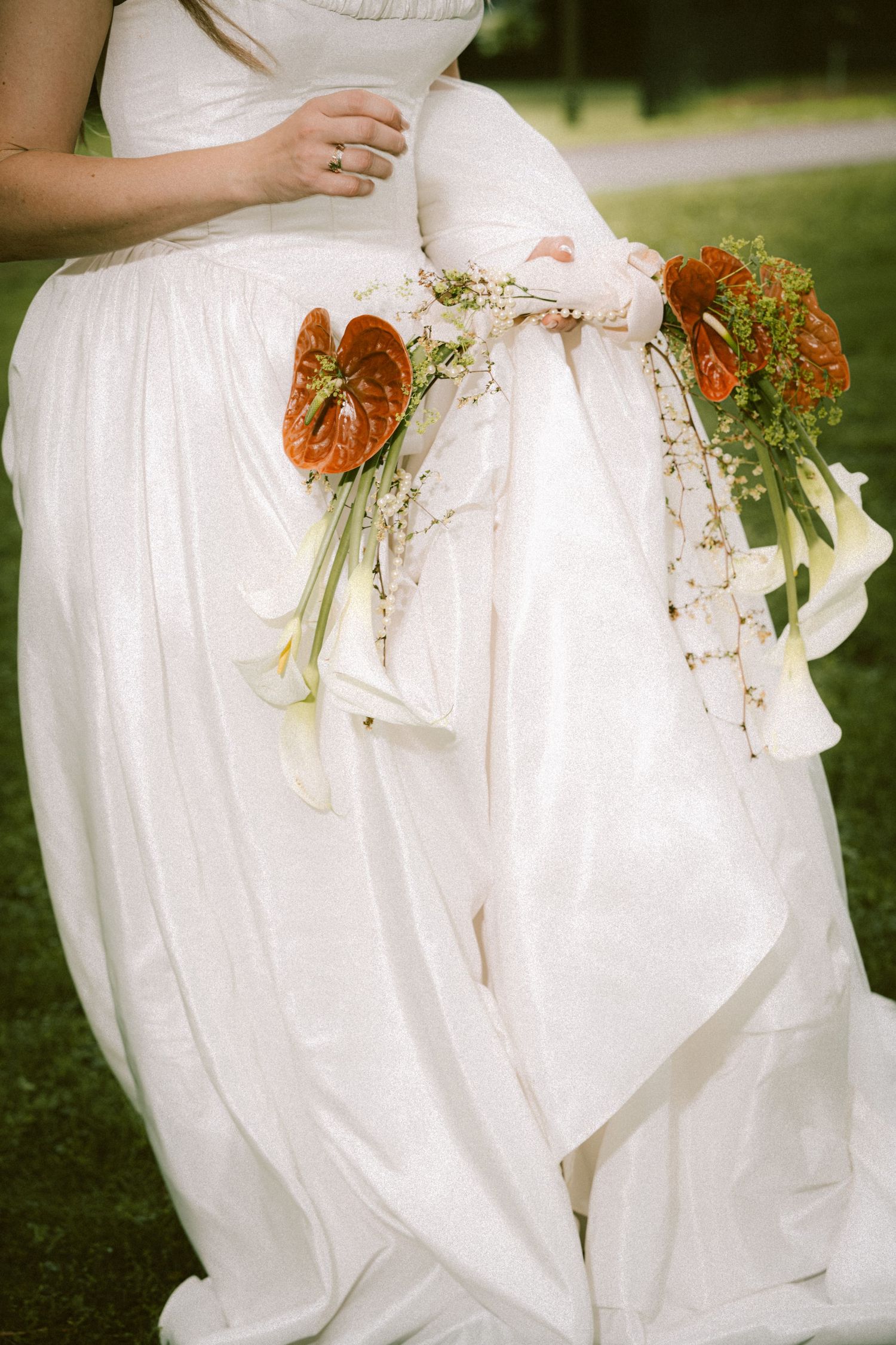Close-up of a bride in a flowing white dress holding a bouquet of orange anthuriums and white calla lilies.