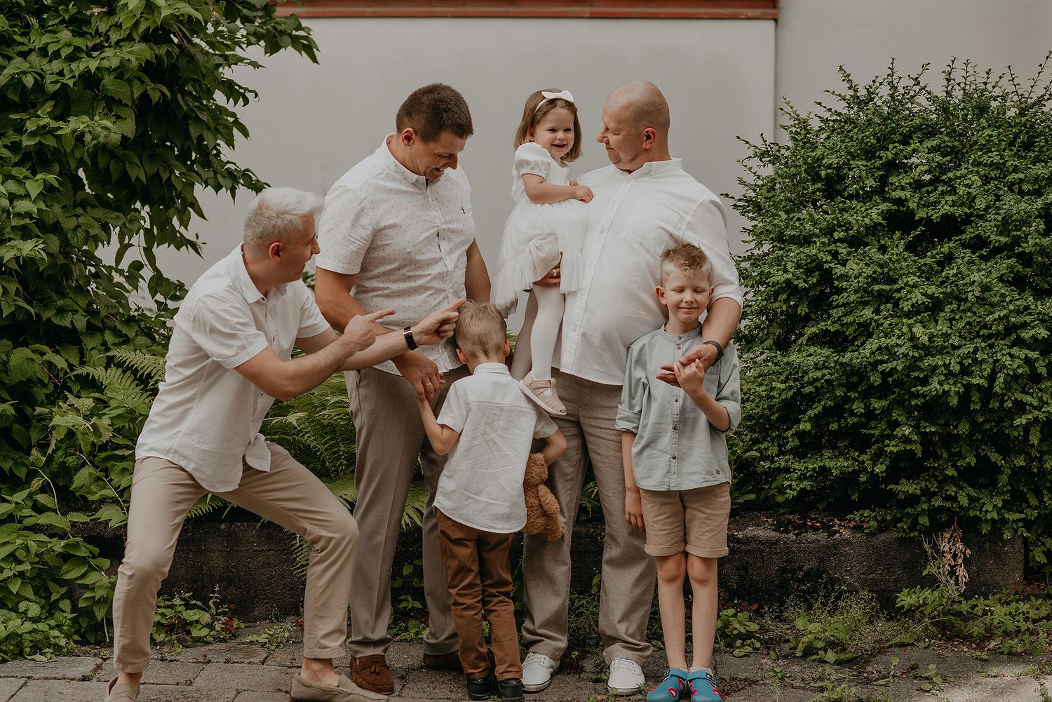 A family in white shirts and khaki pants plays together in a garden setting, creating joyful candid moments.