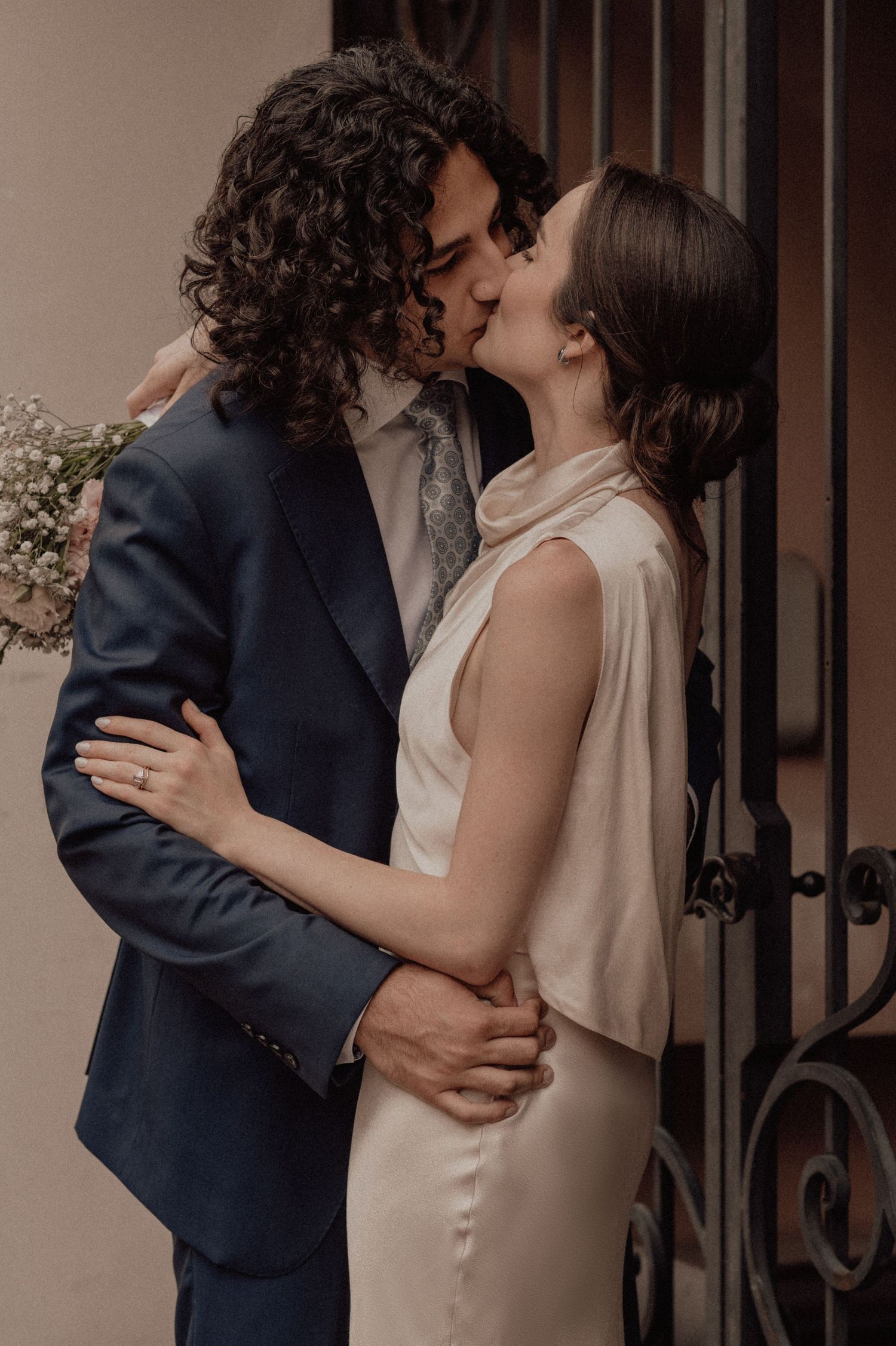 Newlyweds embrace and kiss during their wedding photoshoot against a neutral backdrop.
