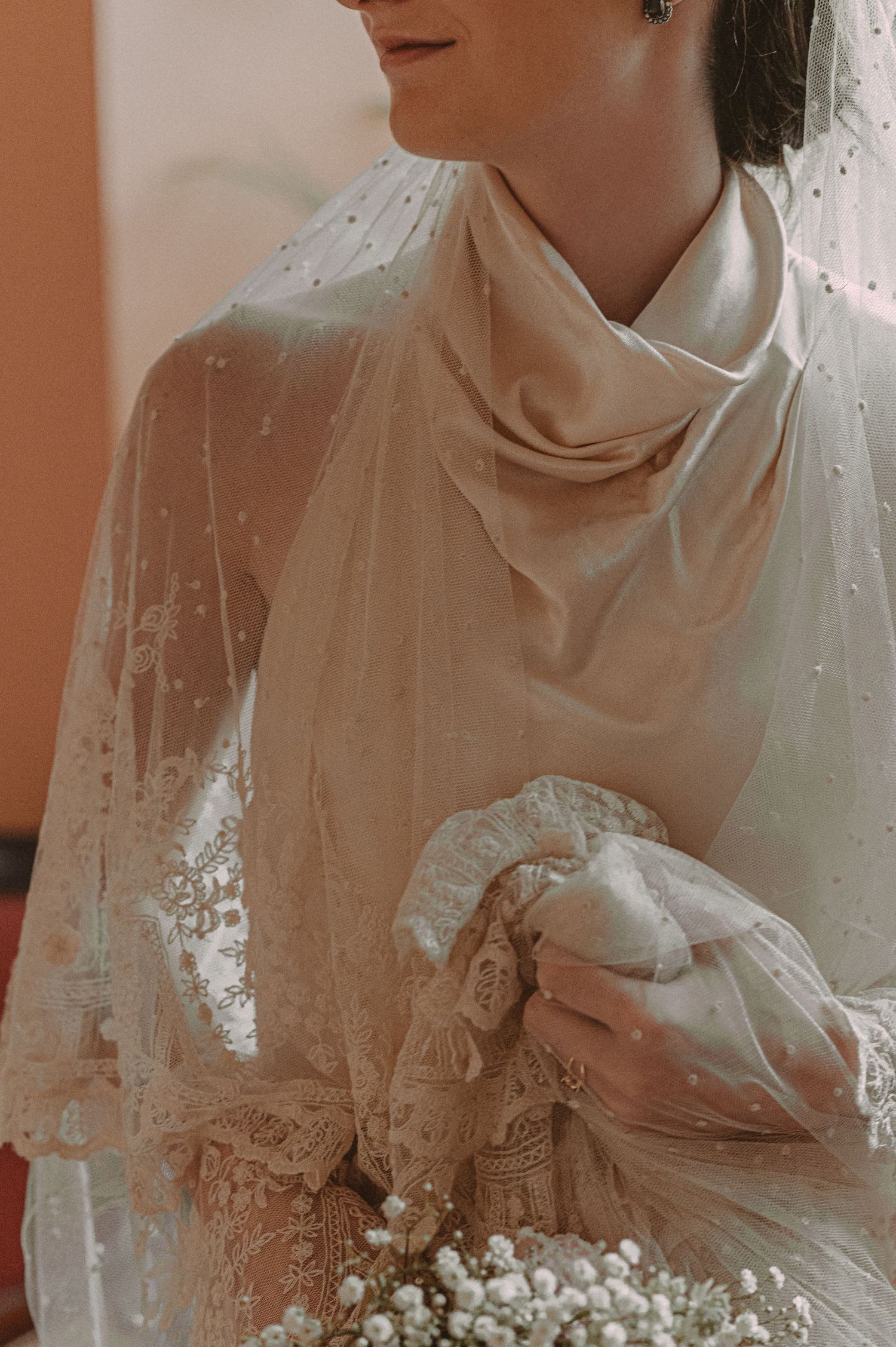 Close-up detail of delicate lace wedding dress with high neckline and draped fabric details.