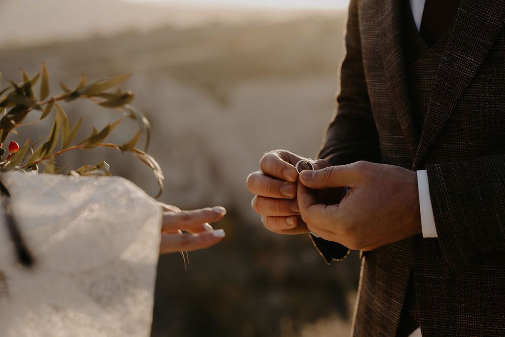 Close-up of groom placing wedding ring on bride's finger during outdoor sunset ceremony.