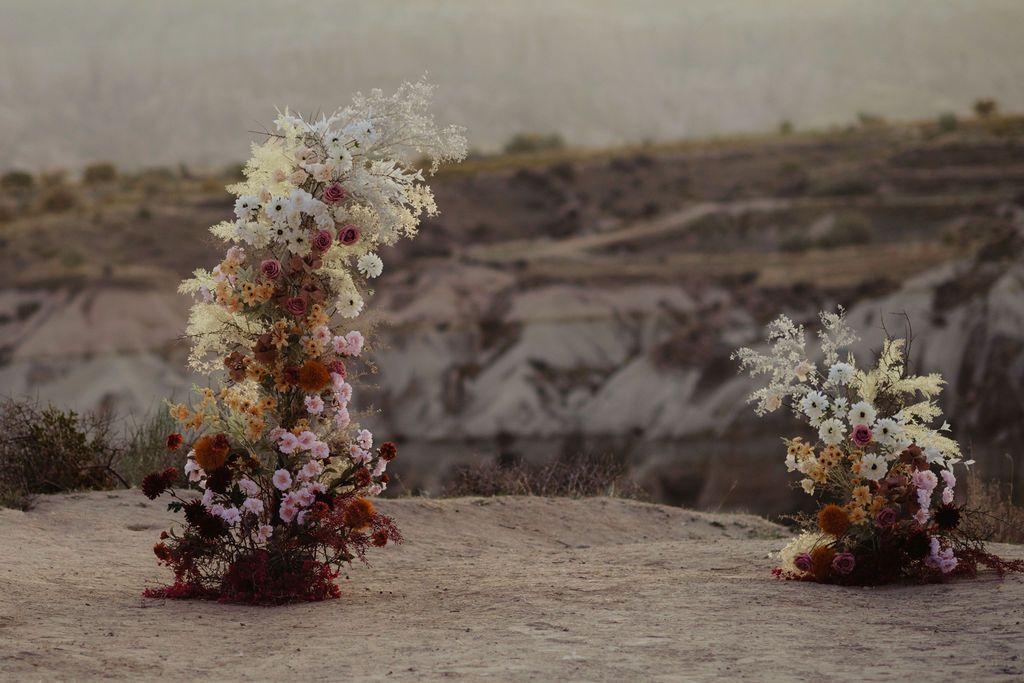 Two wild floral arrangements on rocky desert terrain with misty canyon backdrop.