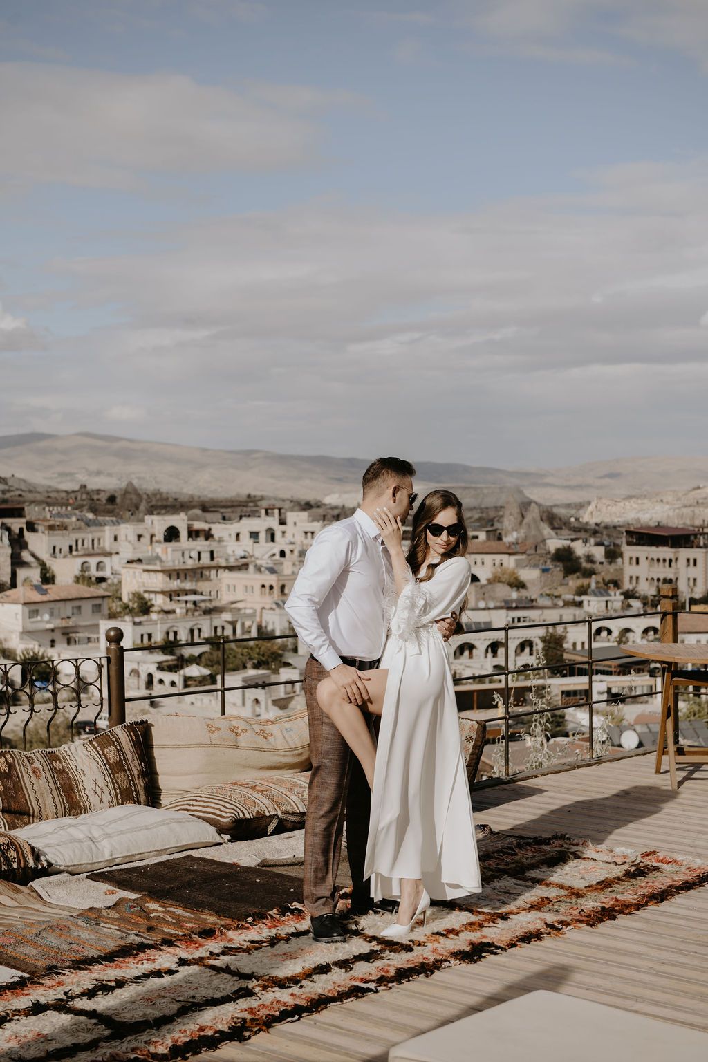 Couple embracing on a rooftop terrace in Cappadocia, Turkey, with cave dwellings and rocky landscape in the background.