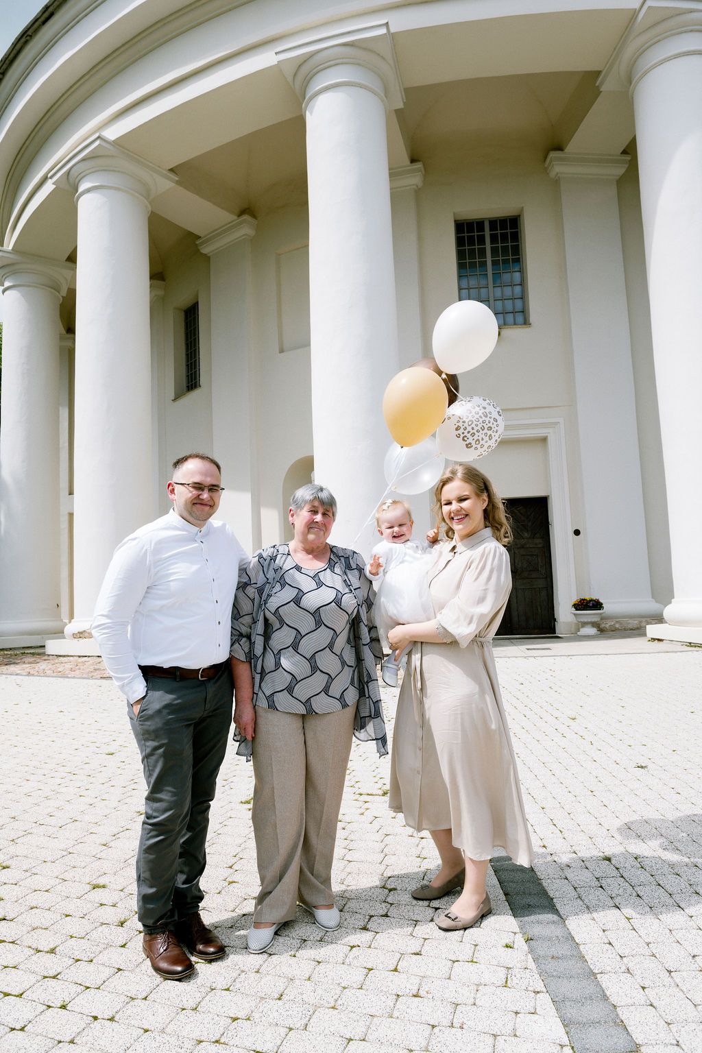 Family of four posing with gold and white balloons outside a white neoclassical building with columns.