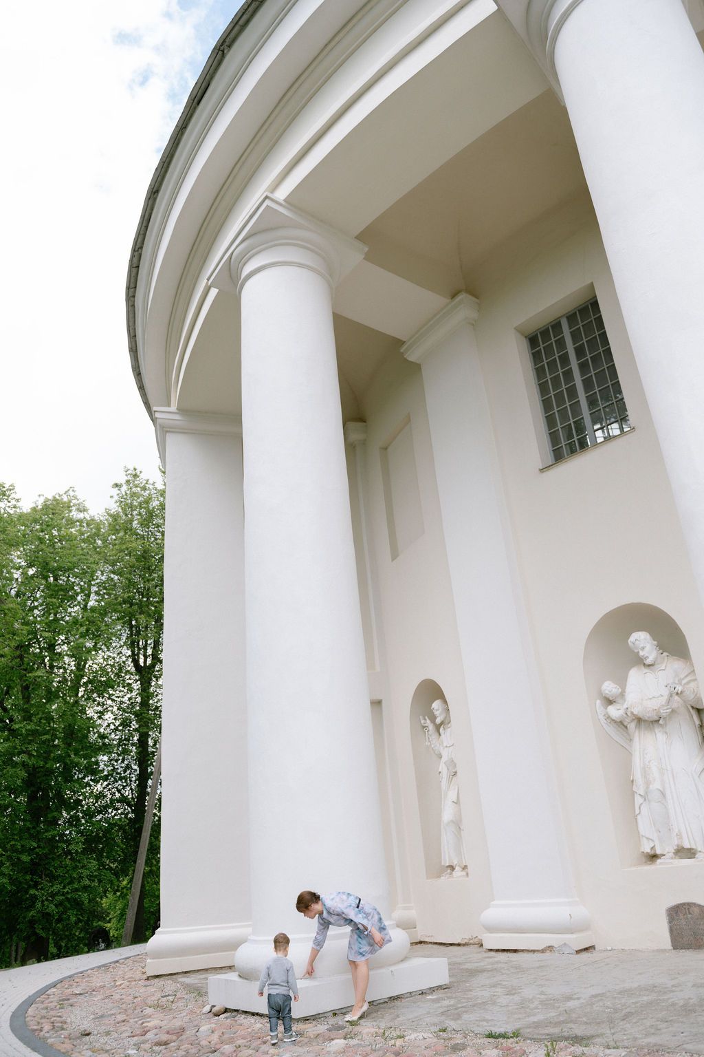 Adult and child stand before a grand white neoclassical building with tall columns and ornate statues in niches.