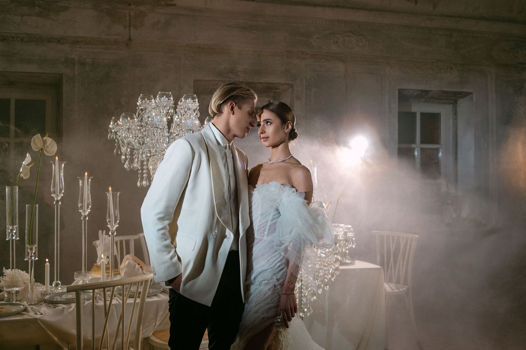 Elegant couple in formal attire sharing a romantic moment in a misty, candlelit reception hall.