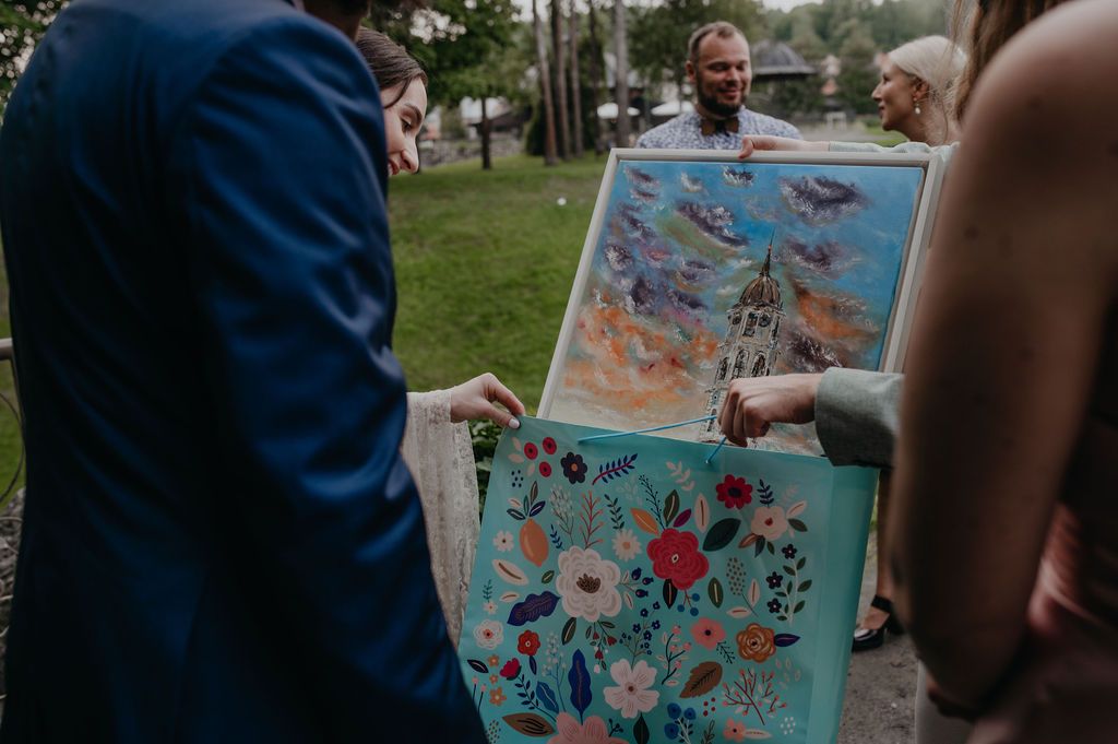 Wedding guests admire colorful floral and abstract paintings outdoors during a wedding celebration.