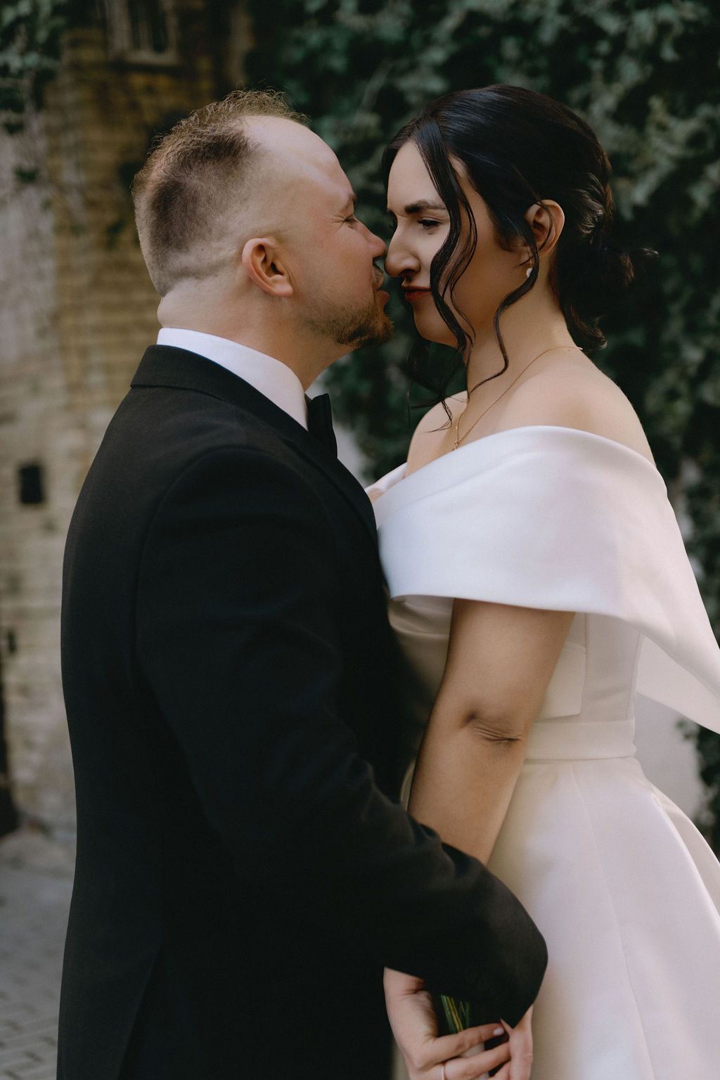 Bride and groom share a romantic moment in an outdoor wedding setting, with the bride in an off-shoulder white gown.