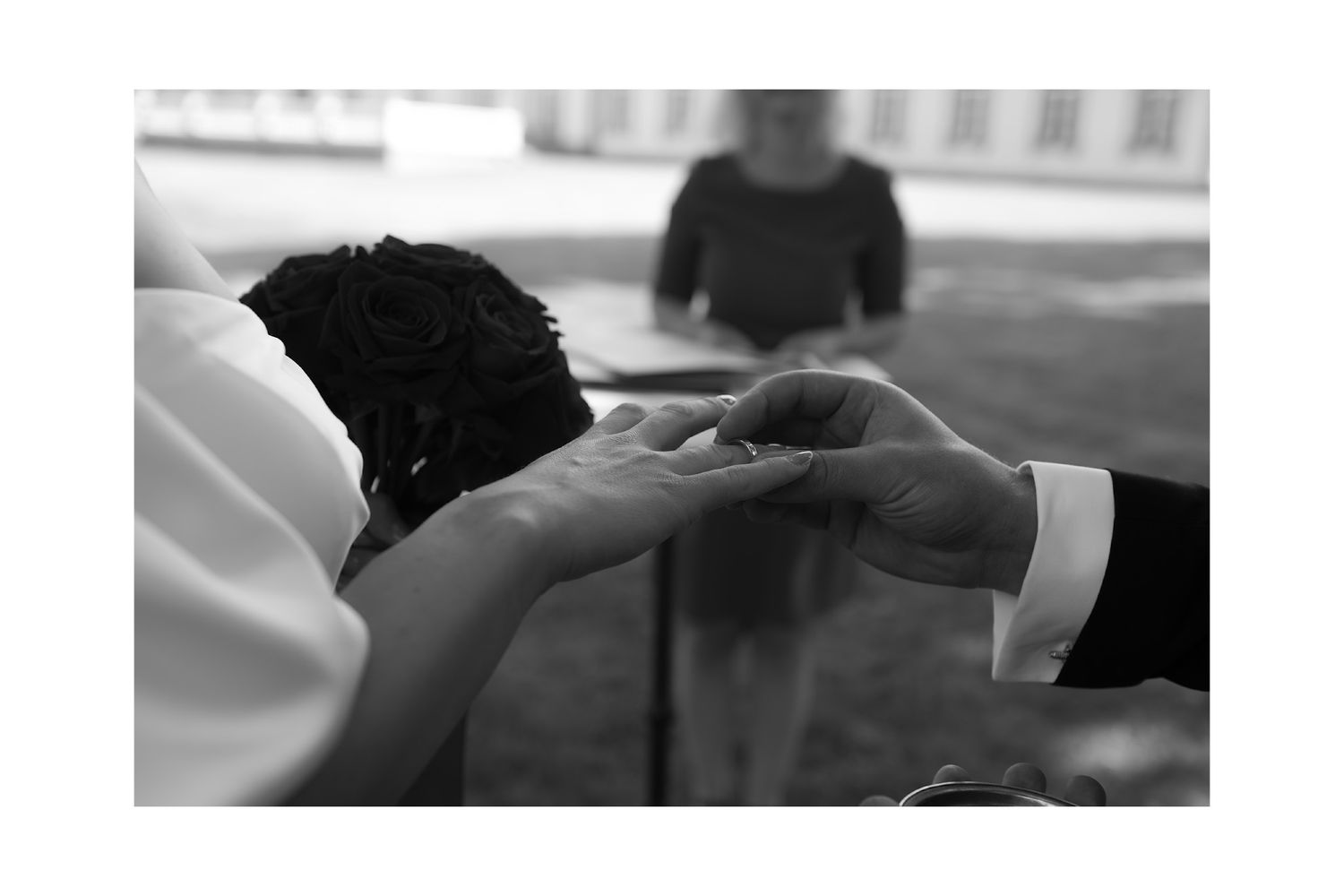 A black and white photo of hands exchanging rings during a wedding ceremony.