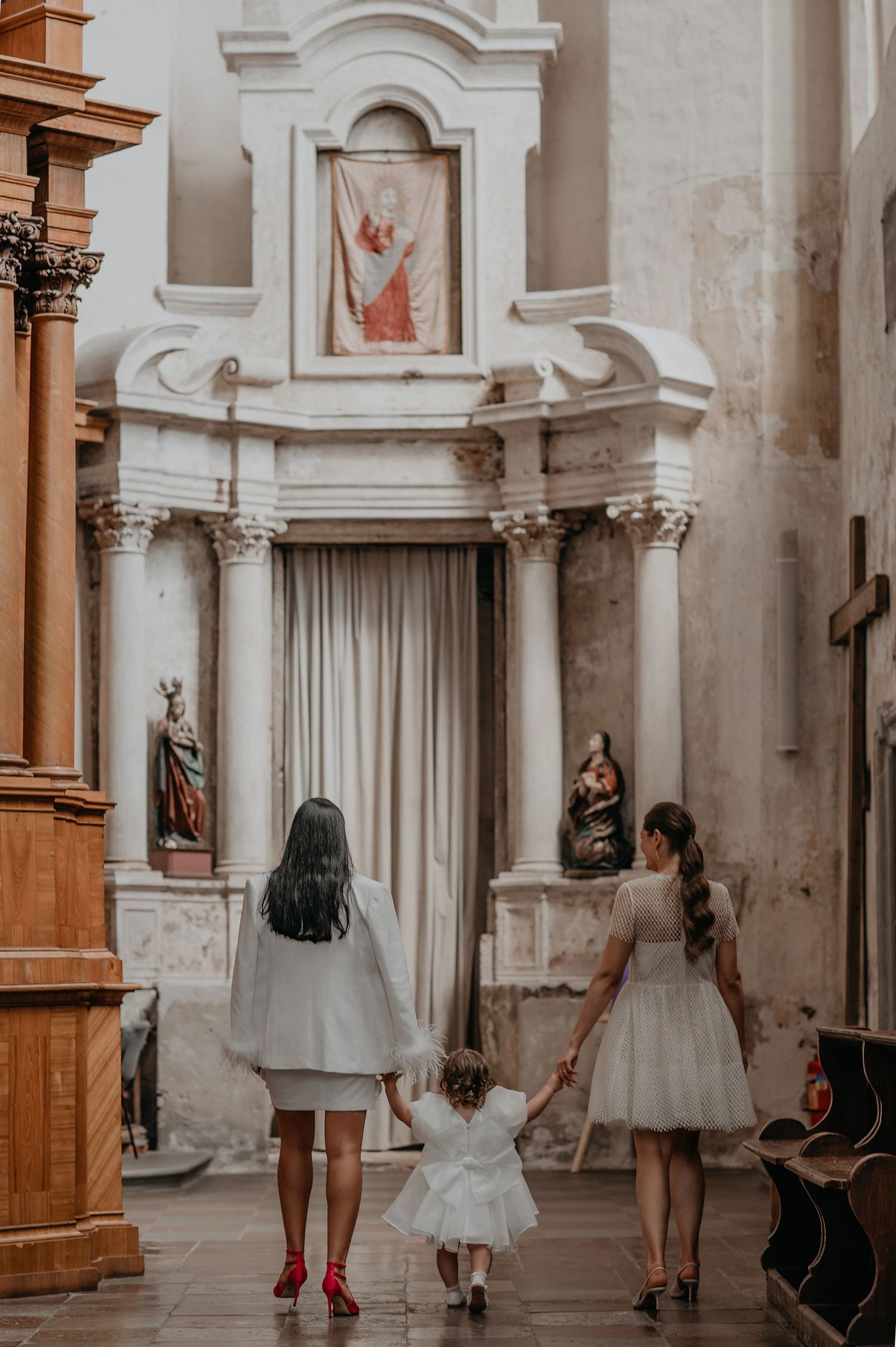 Young dancers in white dresses practice ballet poses in an ornate church hallway with classical architecture.