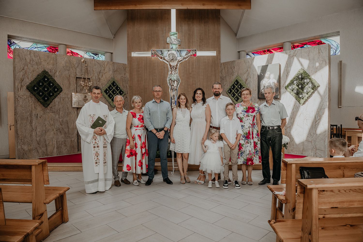A group stands together in a church sanctuary with wooden pews and a crucifix, decorated with red and white accents.