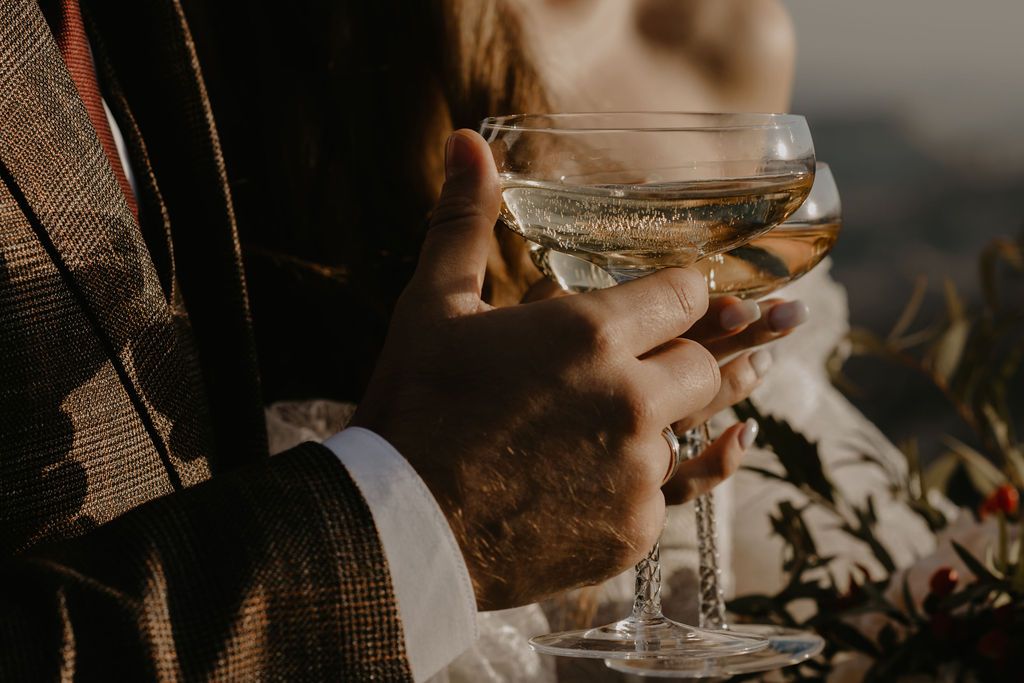 Close-up of couple holding champagne coupe glasses at a wedding celebration in warm golden light.