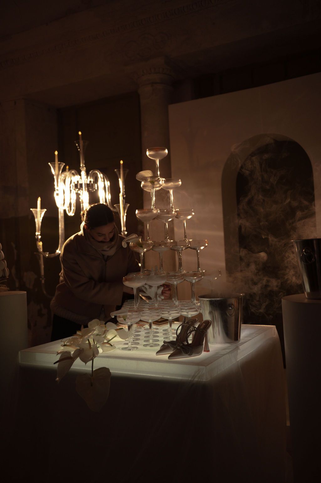 Person arranging a champagne tower display with dry ice smoke effects at an elegant dimly lit event.