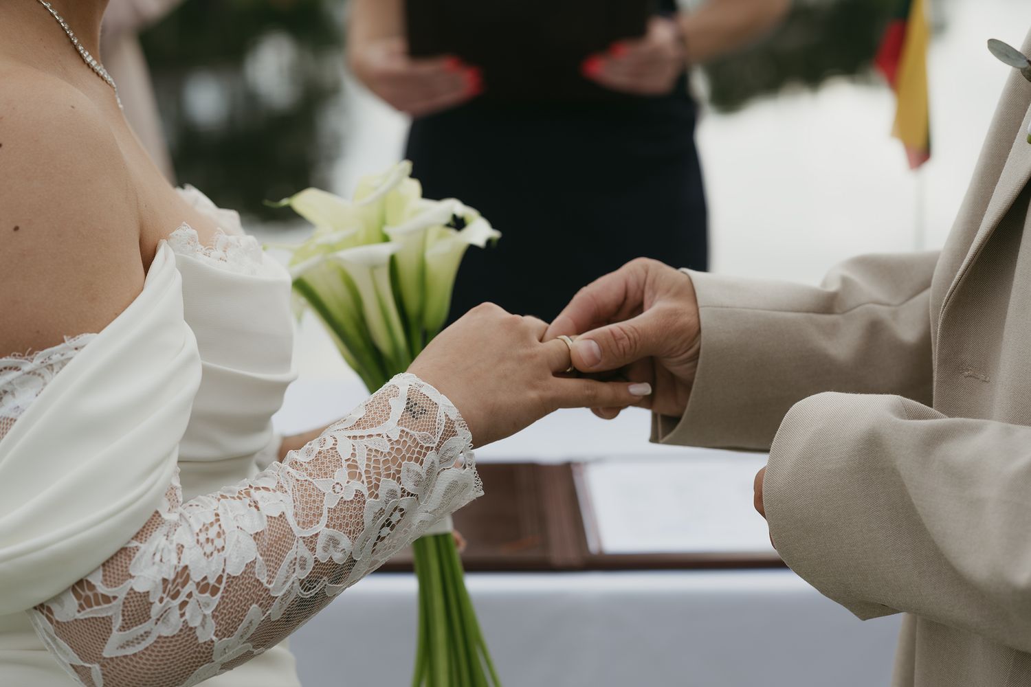 A close-up detail shot of delicate white lace on a wedding dress sleeve with hands visible in the background.