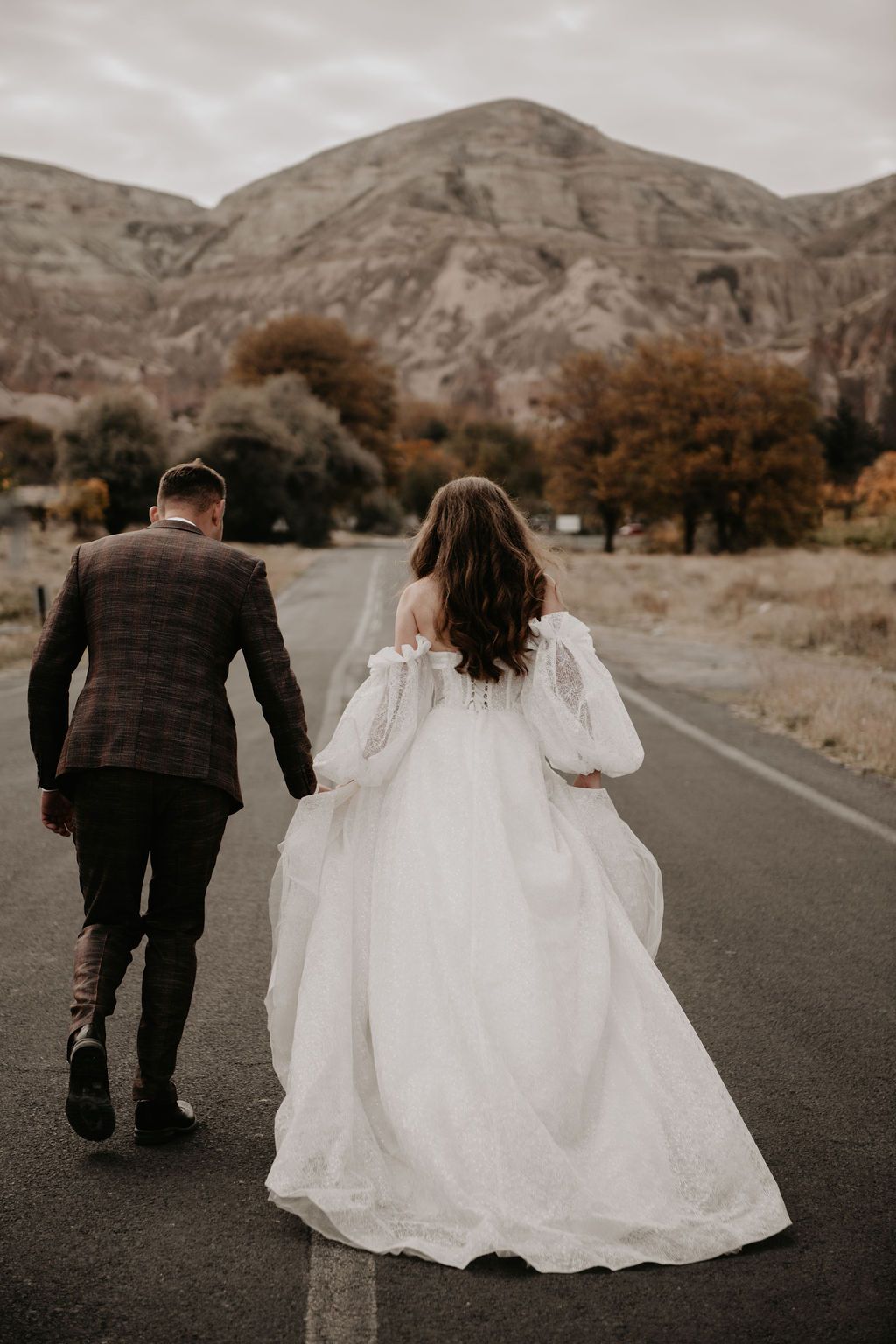 Bride and groom walking hand in hand down a road with mountains in the background on their wedding day.
