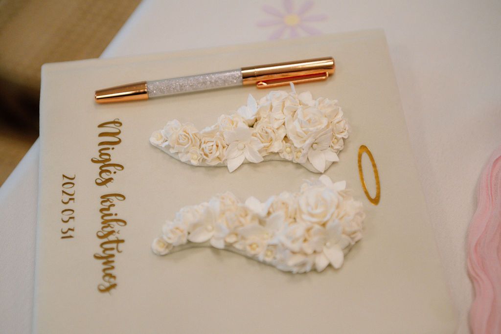 White baptism guest book with gold pen, white flower decorations, and angel wings motif on a light background.