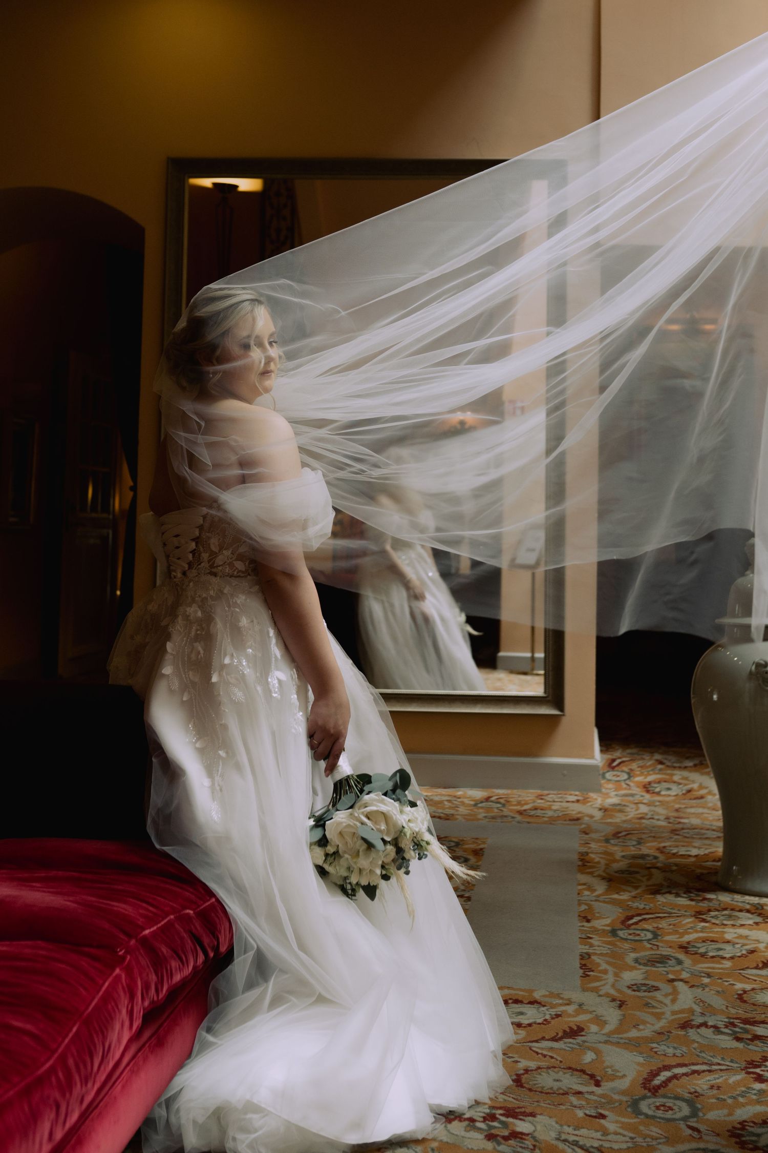 A flowing white wedding veil creates an ethereal motion effect as it billows around a bride in a wedding gown.