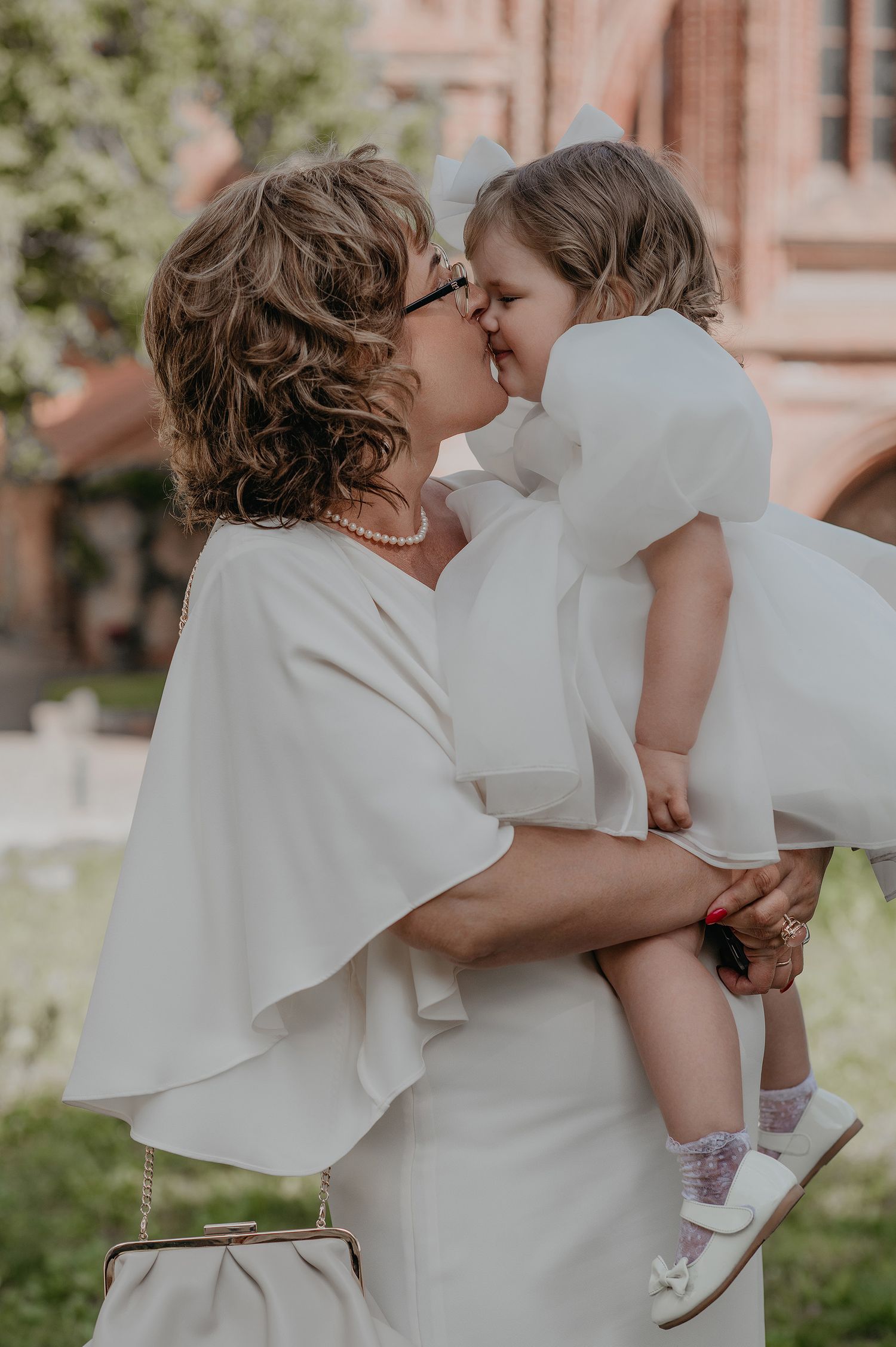 A tender moment captured between a parent and child in matching white outfits against a soft brick backdrop.