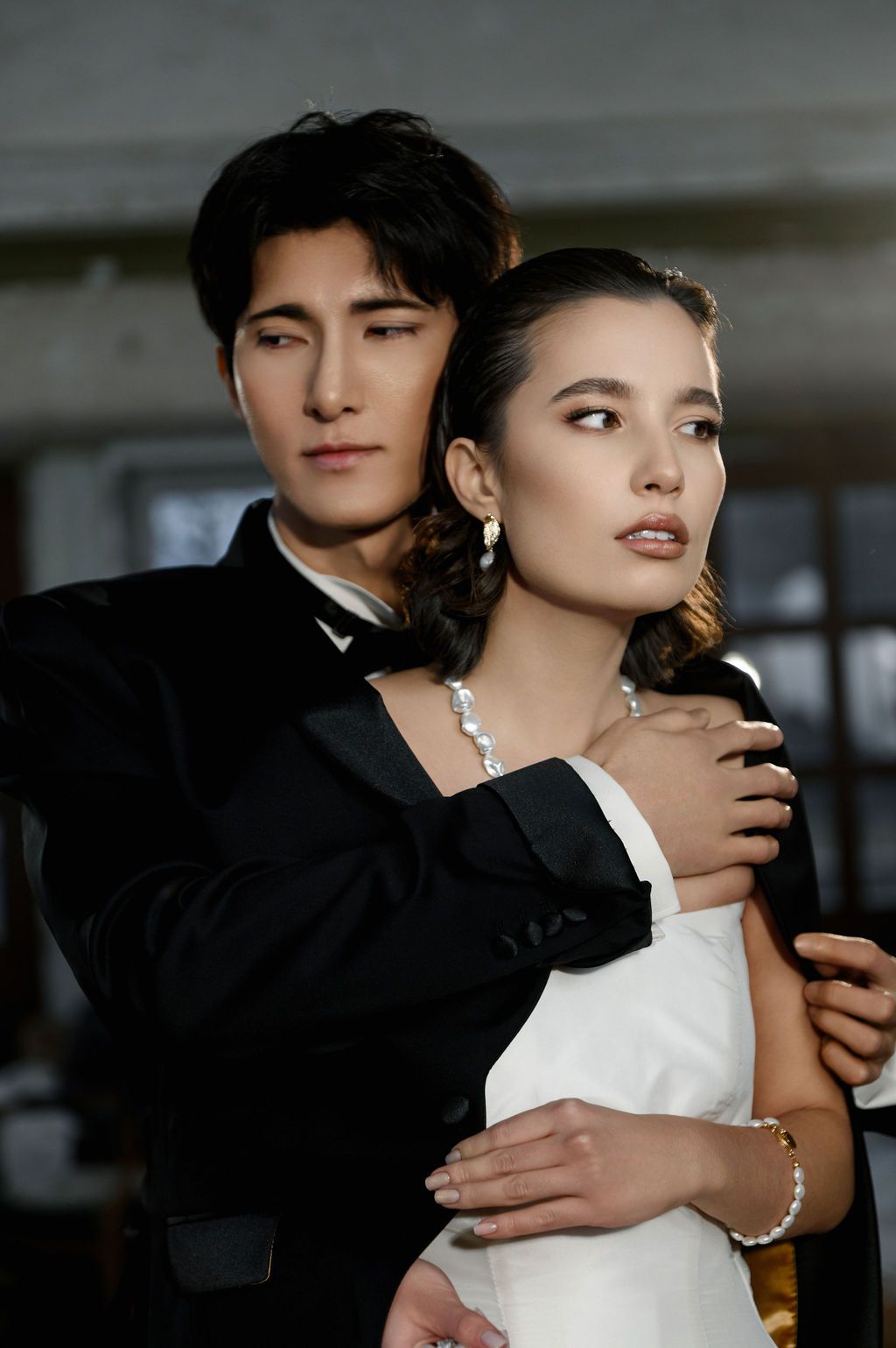 Stylish couple in formal black and white attire posing together in an elegant indoor setting.