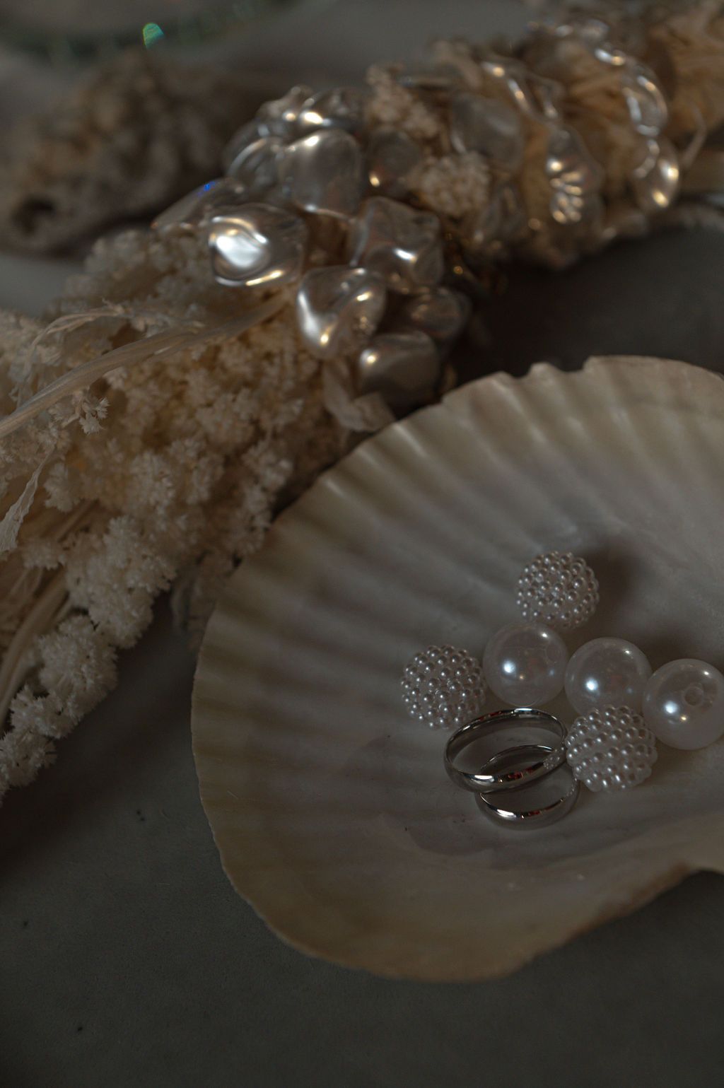 Seashells with pearl beads and a silver ring arranged on a scallop shell display.