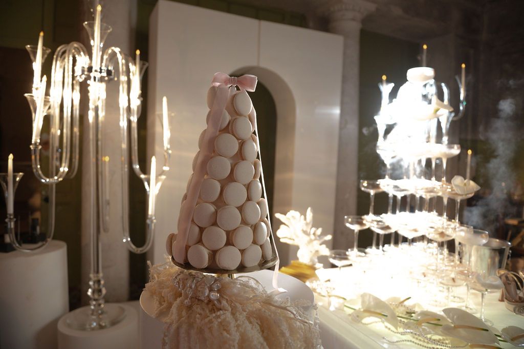Elegant macaron tower wedding cake display with champagne glasses pyramid and candelabras in soft romantic lighting.