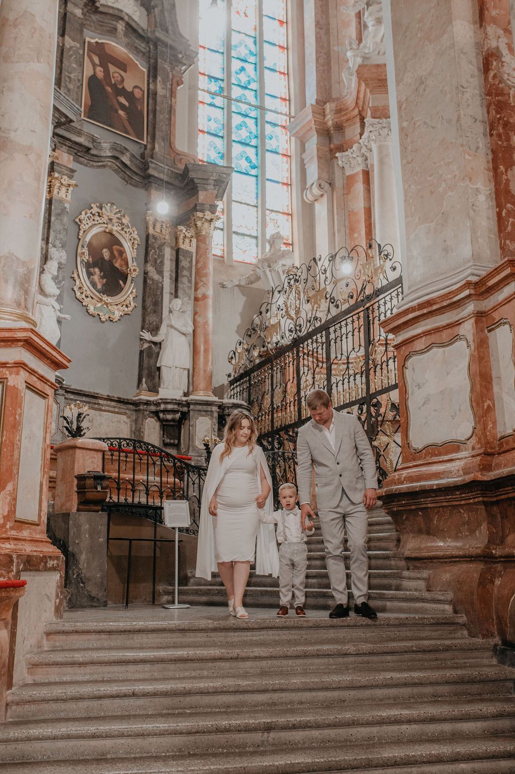 Family in formal attire descending ornate baroque church stairs, with elegant railings and classical paintings in background.