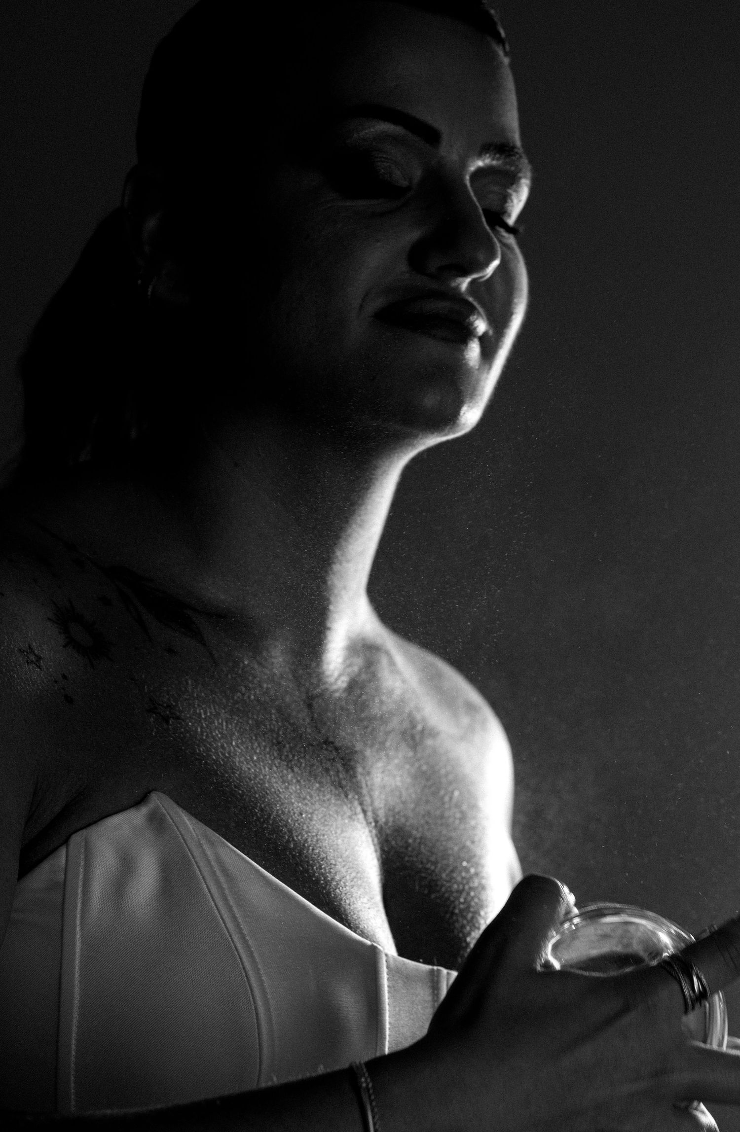 Black and white portrait of a bride in a white corset dress with her eyes closed as a fine perfume mist falls around her.