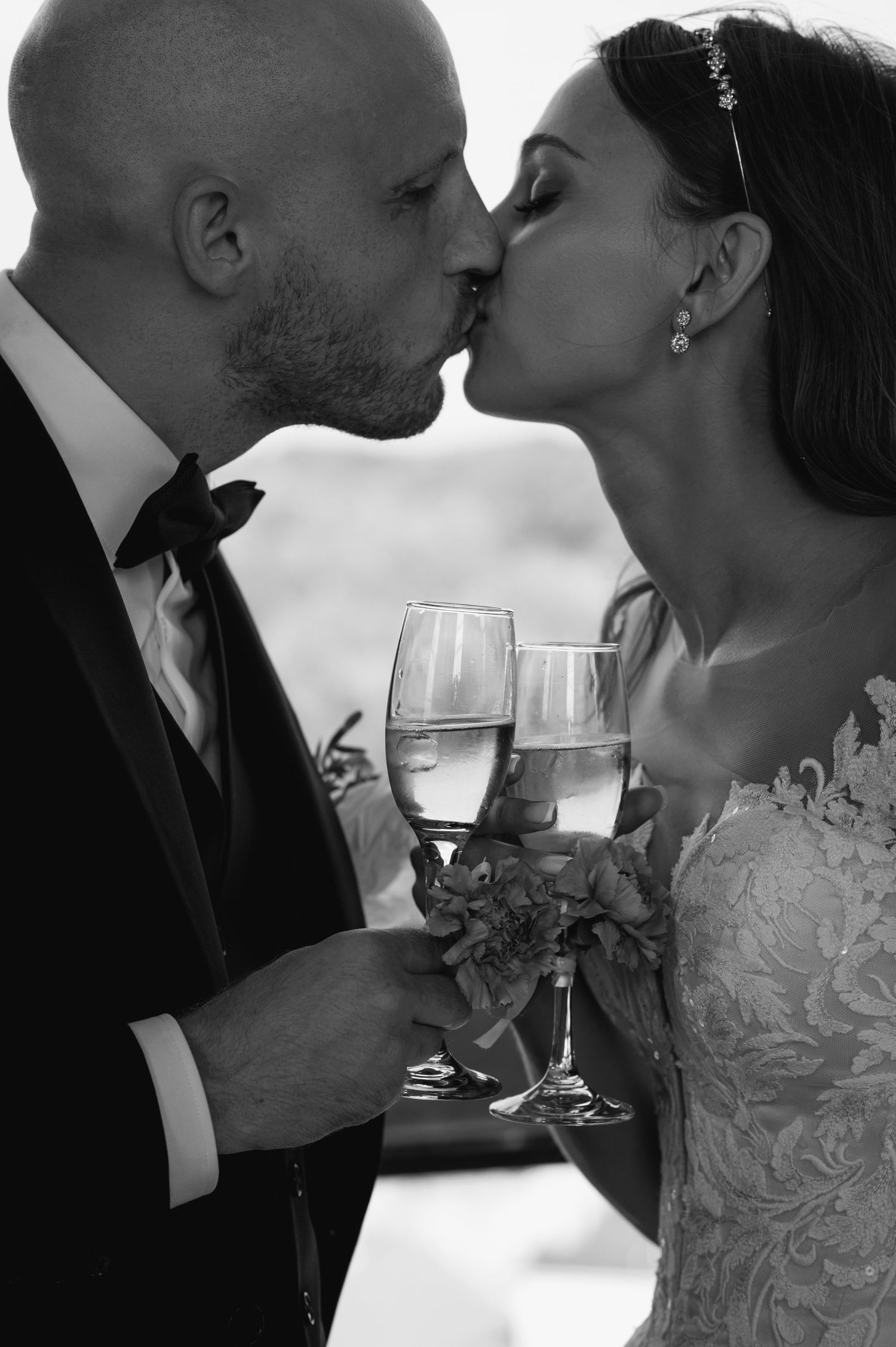 A romantic black and white photo sequence of a couple kissing while holding wine glasses at a wedding celebration.