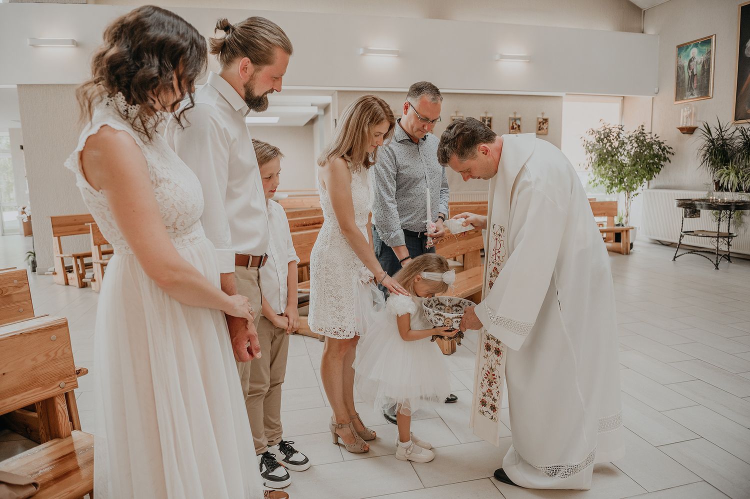 A group of people in white outfits dance together on a light wooden floor during a celebration.