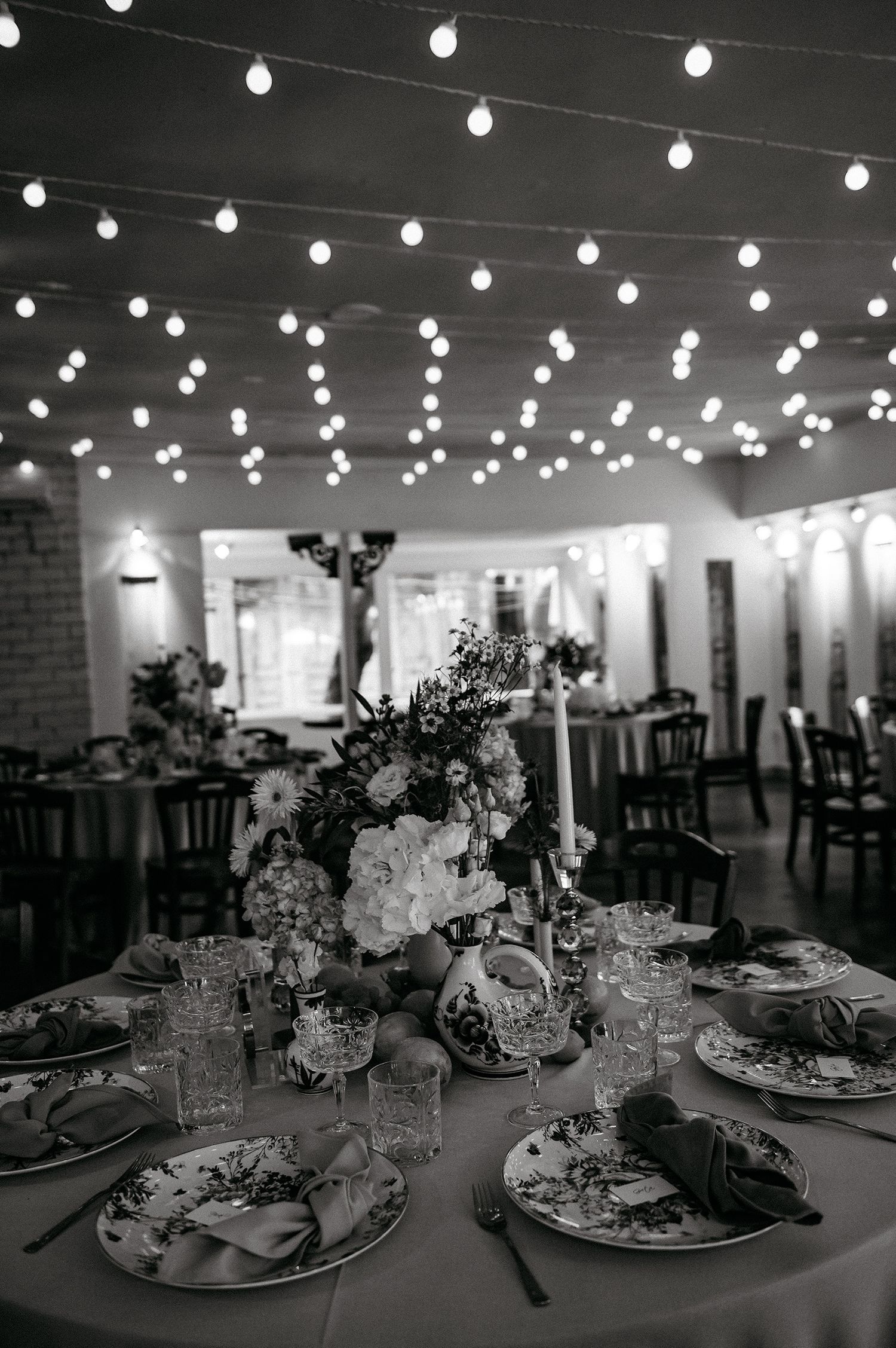 Elegant wedding reception tables set with string lights overhead creating a romantic ambiance in black and white.