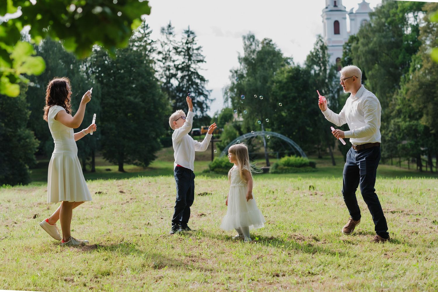 Wedding couple dances joyfully in a sunlit meadow with trees in the background.