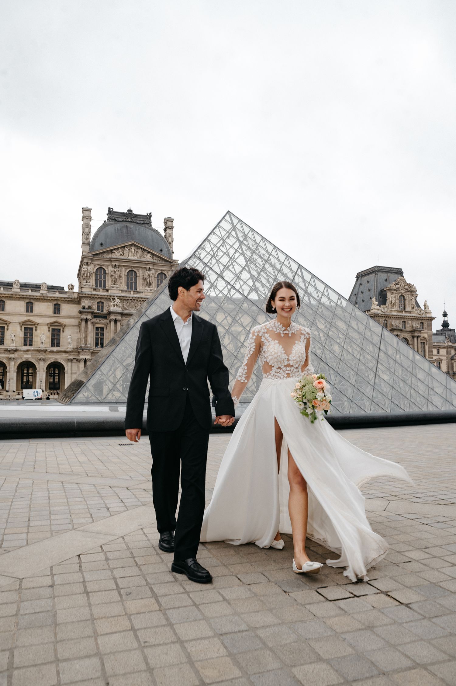 A couple poses for wedding photos in front of the iconic glass pyramid at the Louvre Museum in Paris.