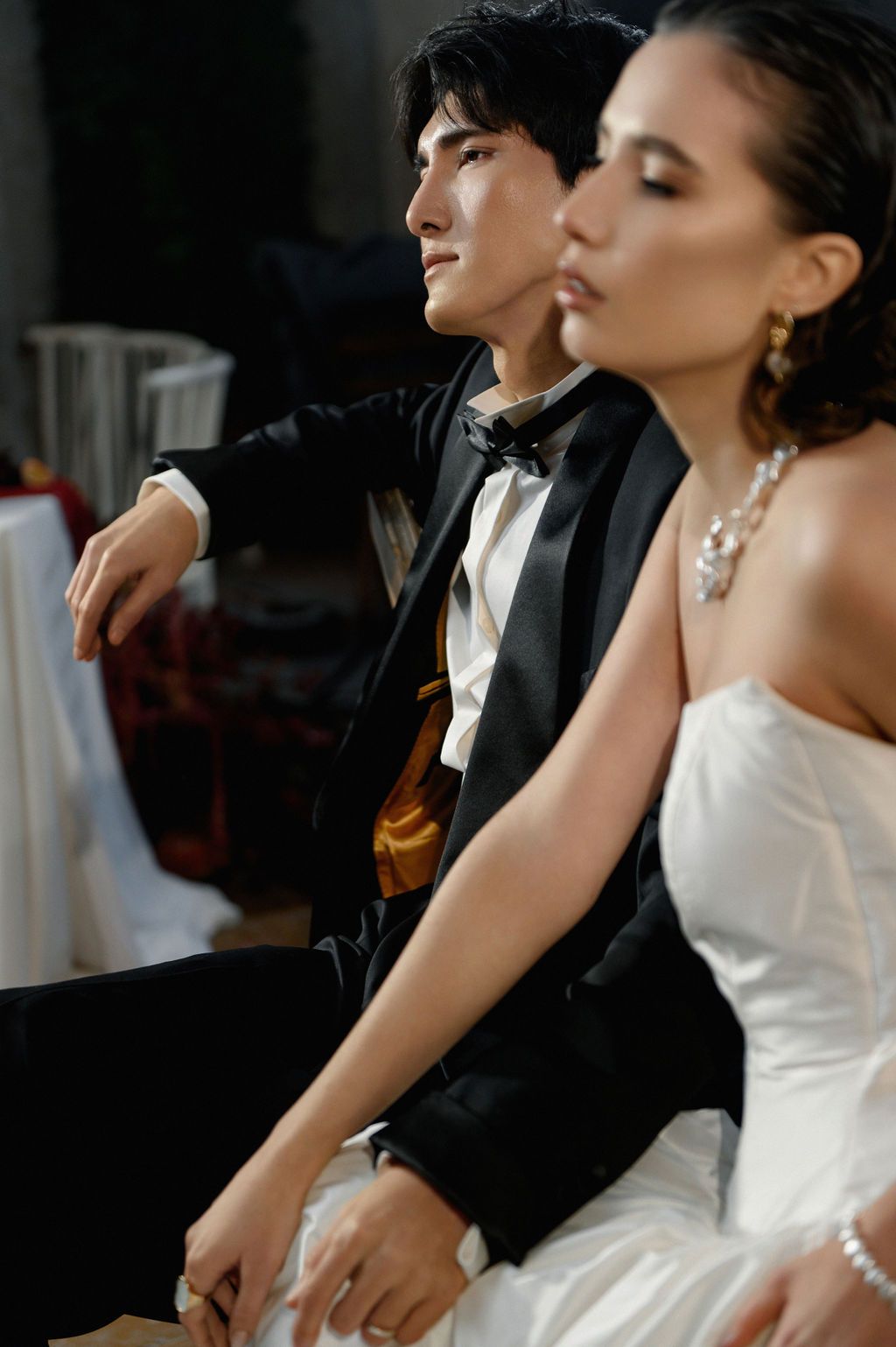 A groom in a black tuxedo and bride in a white strapless gown sit together at their wedding reception.