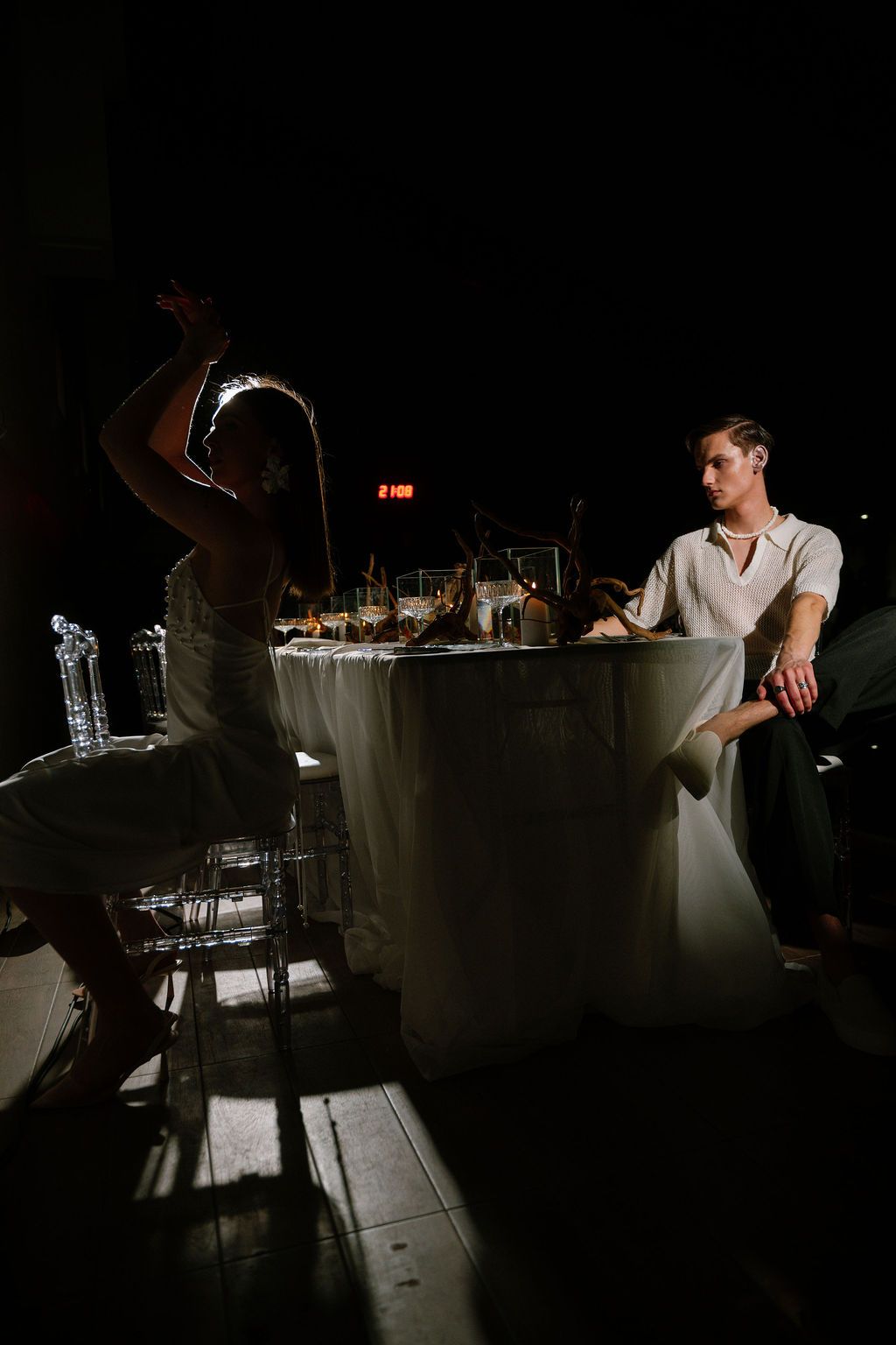 A man and woman share an intimate moment at a dimly lit banquet table during an elegant evening event.