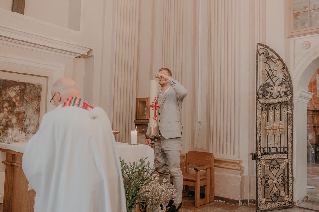 Man in gray suit speaking at church altar during religious ceremony with ornate iron gate.