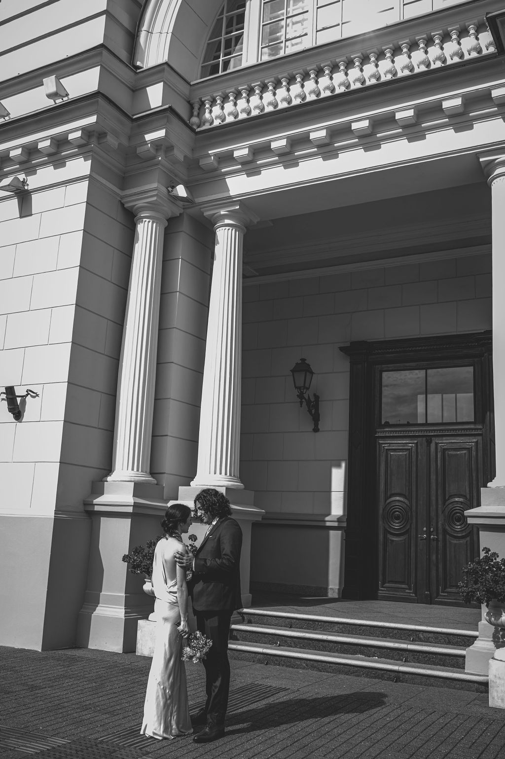 Bride and groom share a romantic moment outside a neoclassical building with tall columns in a black and white wedding photo.