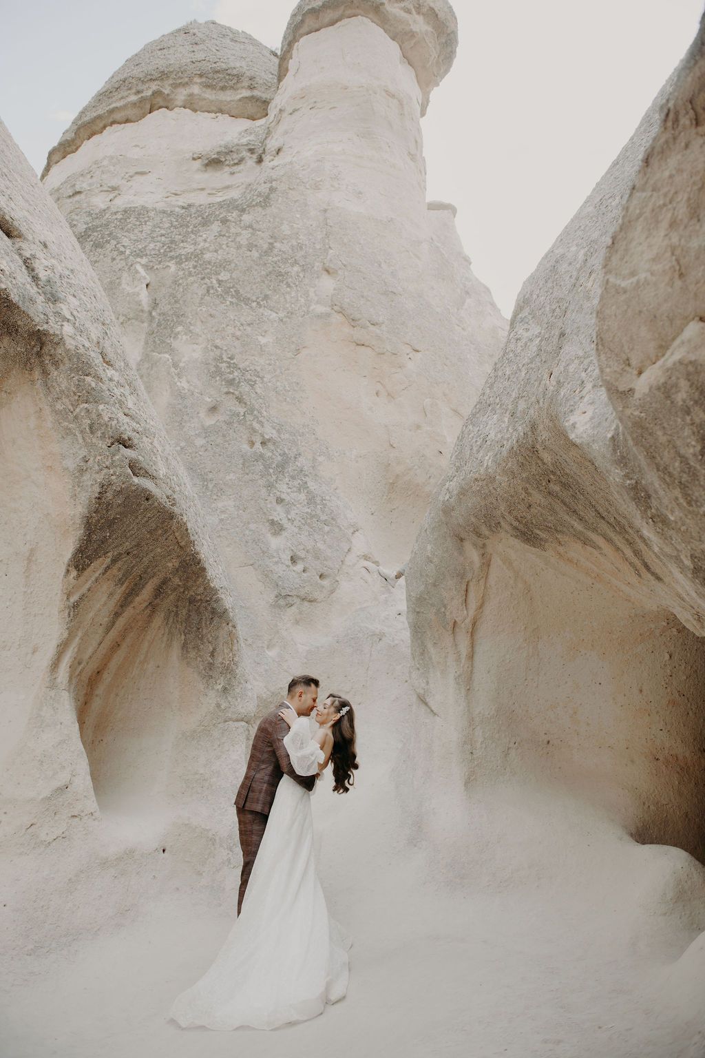 Couple shares a romantic kiss in a stunning white rock canyon, bride in flowing gown, groom in brown suit.