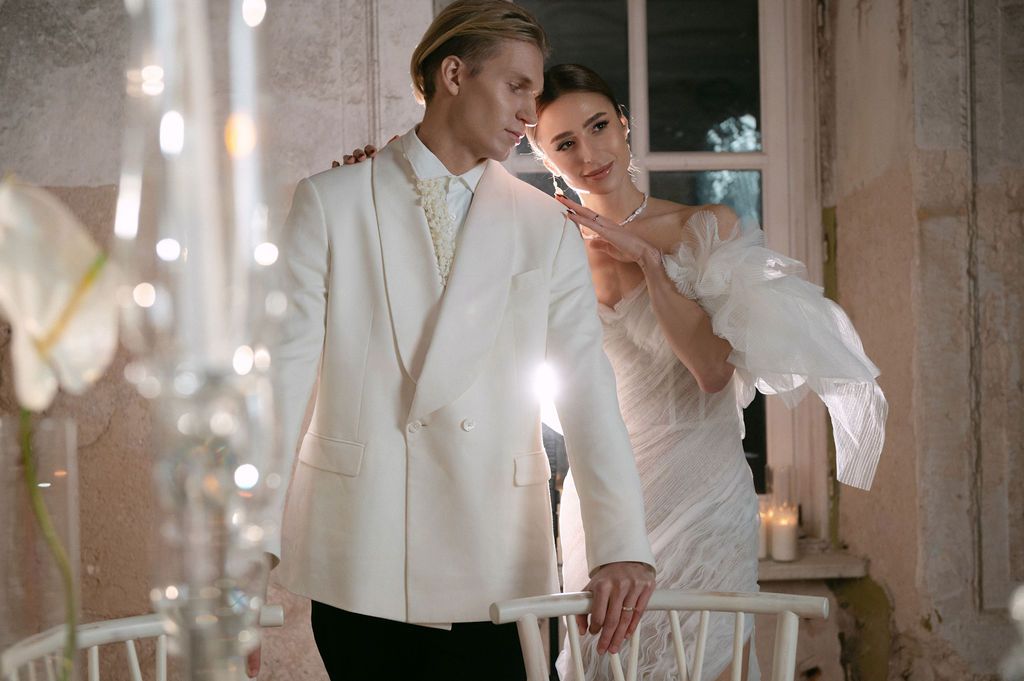 Elegant couple in white wedding attire lighting a candle together at a romantic reception venue.