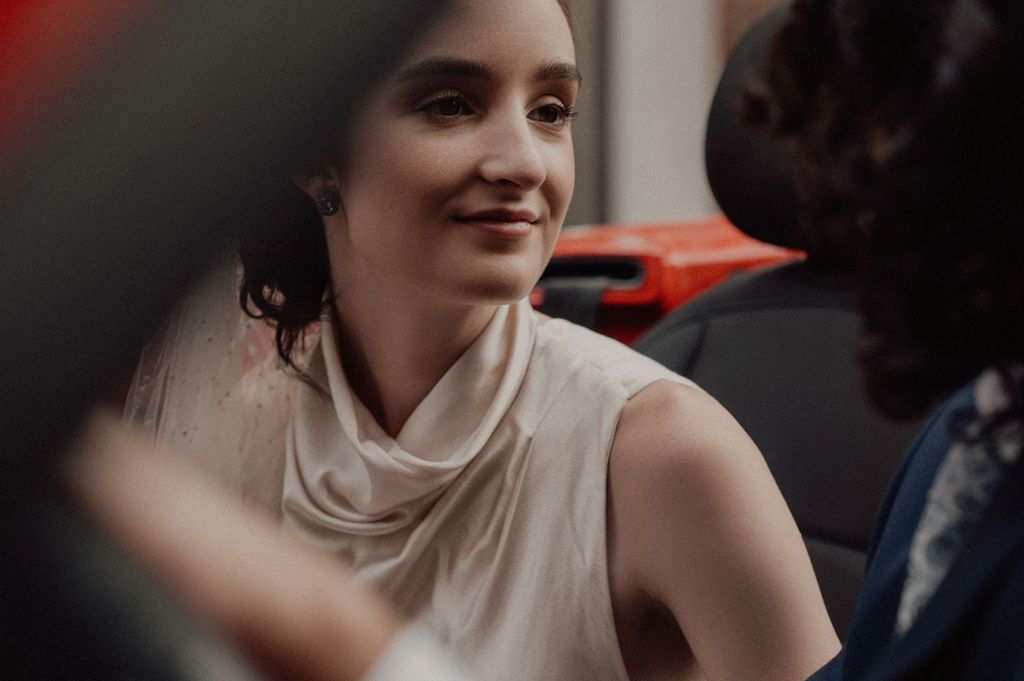 A young woman in a white sleeveless top smiles warmly during an elegant event, with soft bokeh background lighting.