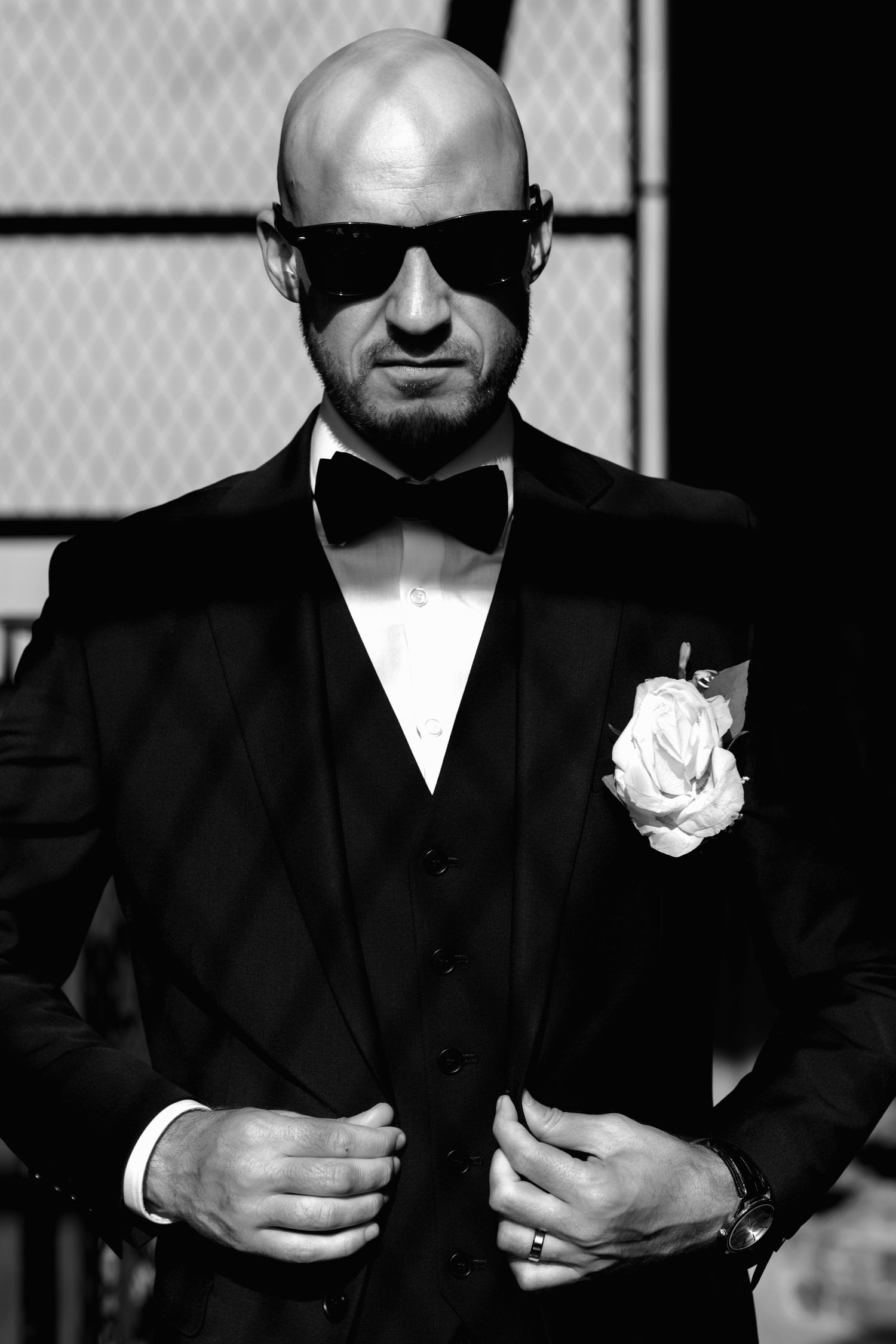 A dramatic black and white photo series showing a person in a dark suit with a white boutonniere against a shadowy background.