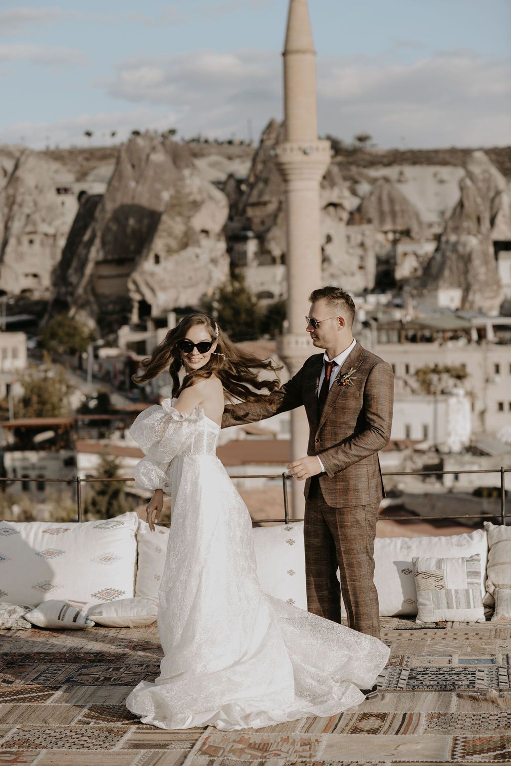 Bride and groom dancing on a rooftop terrace in Cappadocia, Turkey, with iconic fairy chimneys and a minaret backdrop.