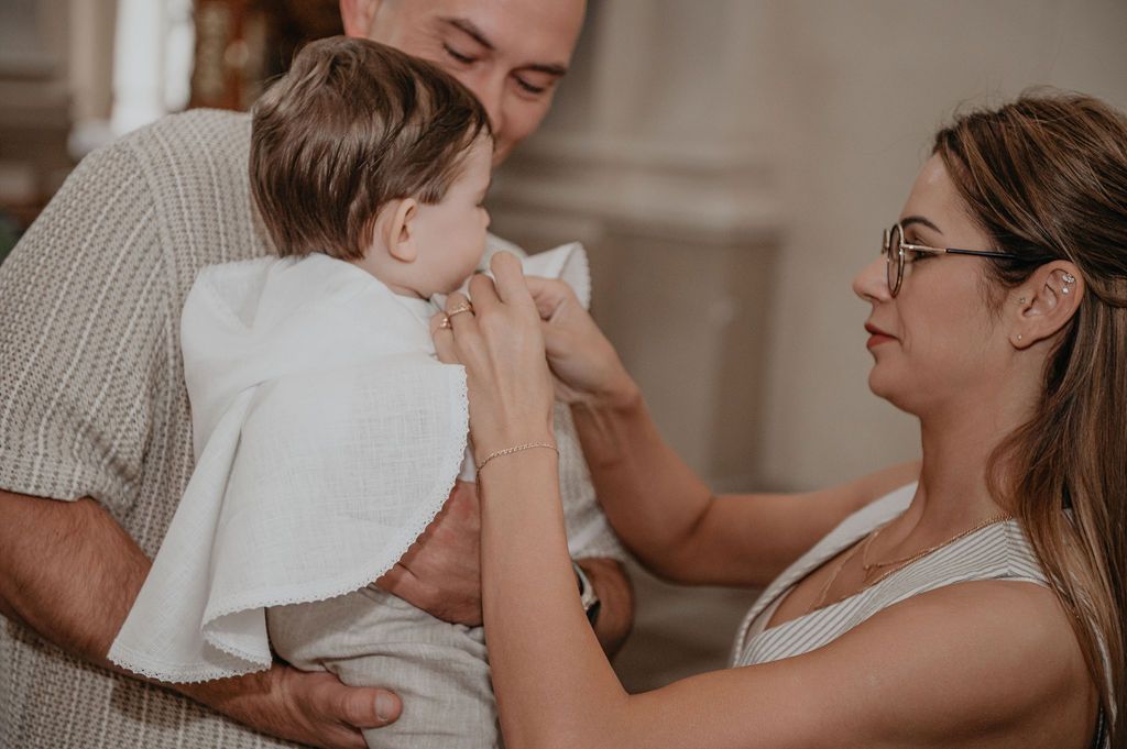 Parents tenderly caring for their baby wrapped in a white cloth during a baptism ceremony.