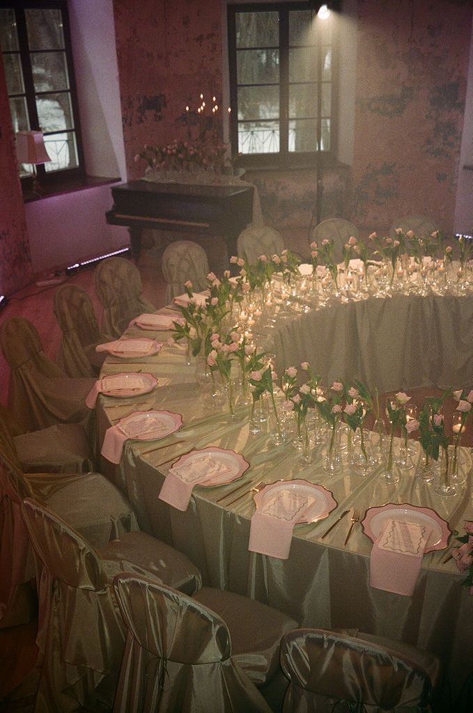 Elegant wedding reception table with green linens, pink tulips, candles, and white place settings in a romantic venue.