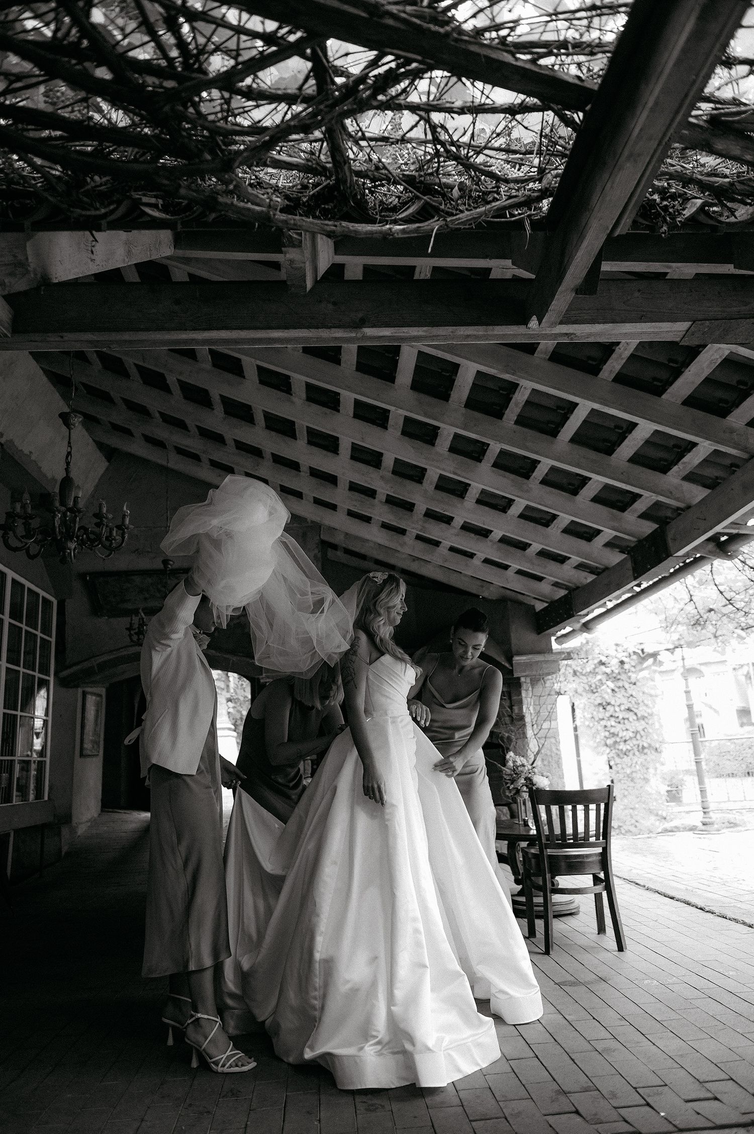 Black and white wedding photos showing bridal gowns hanging from a covered porch railing in a rustic outdoor setting.