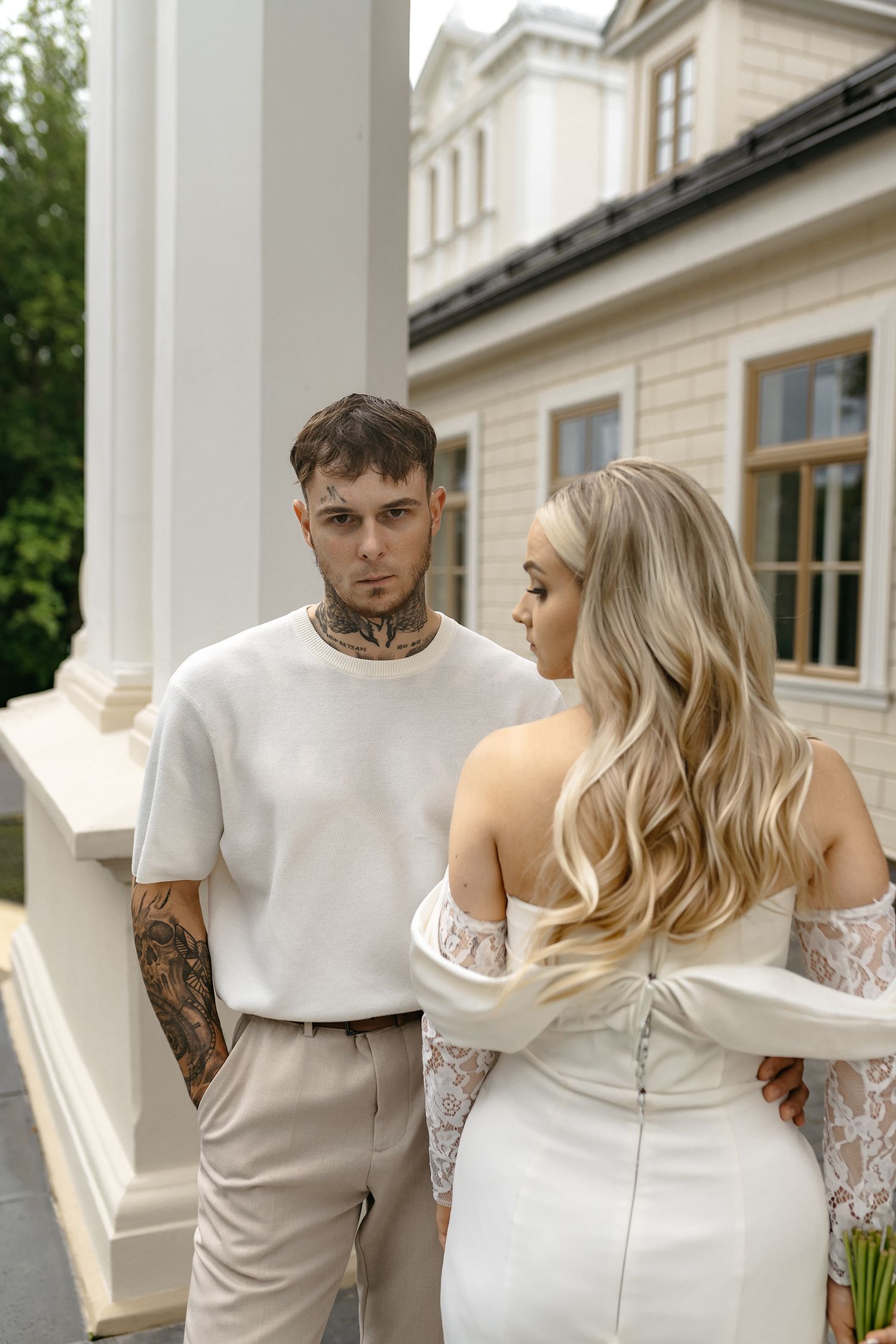 Couple in white wedding attire sharing intimate moments on a balcony of an elegant white building.